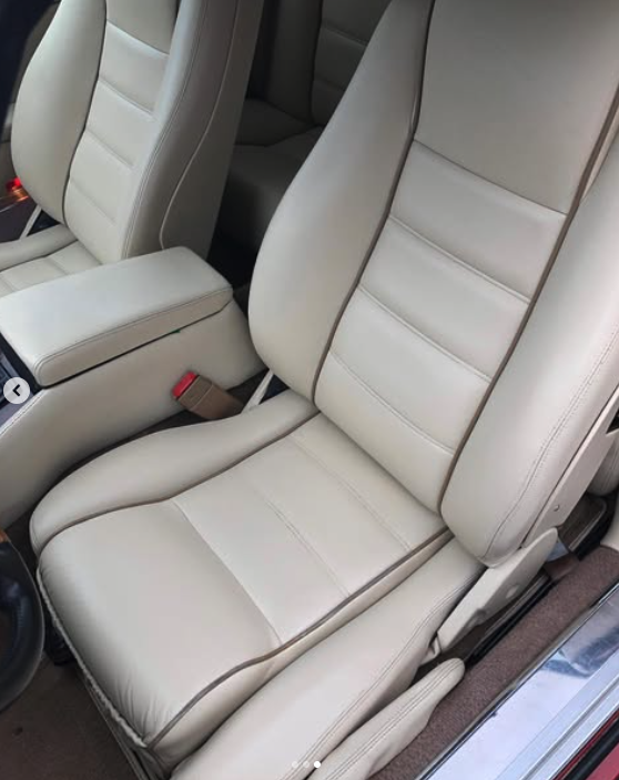 Front passenger seat in a light-colored vehicle interior, showing leather upholstery with stitching, a headrest, and part of the center console and door.