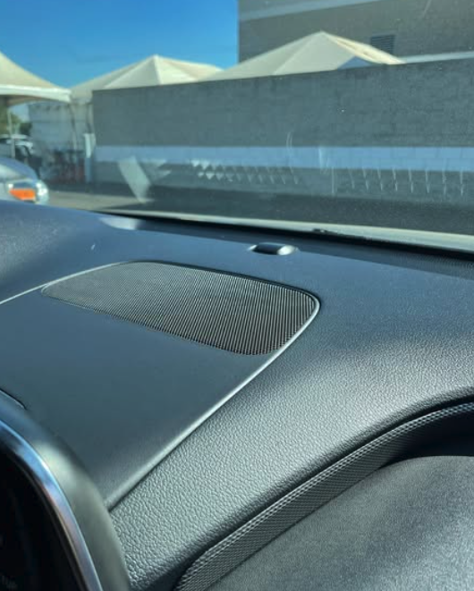 View from inside a car showing the dashboard and windshield with tents and a building visible outside.