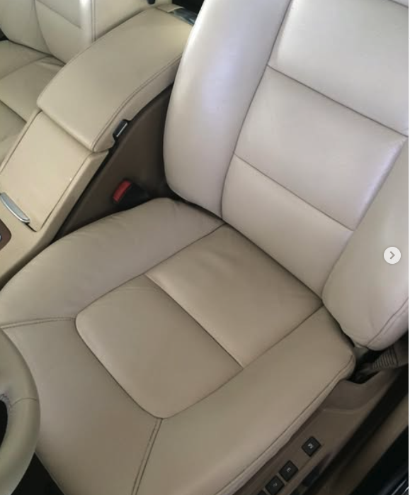 A beige car seat in the driver or passenger side of a vehicle with visible seatbelt buckle and control buttons nearby.