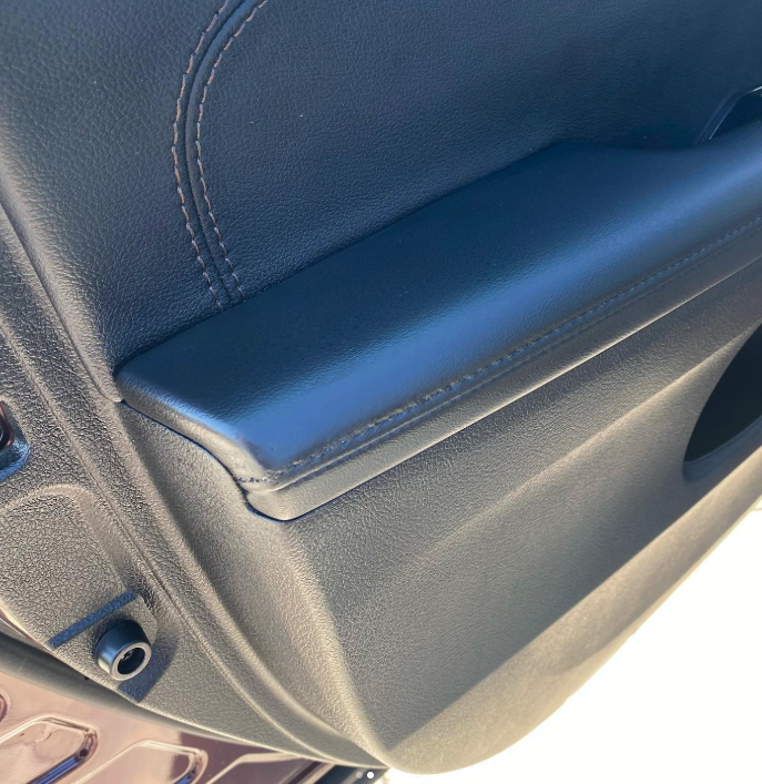 Close-up of a car's interior door panel, featuring a black armrest with stitching.