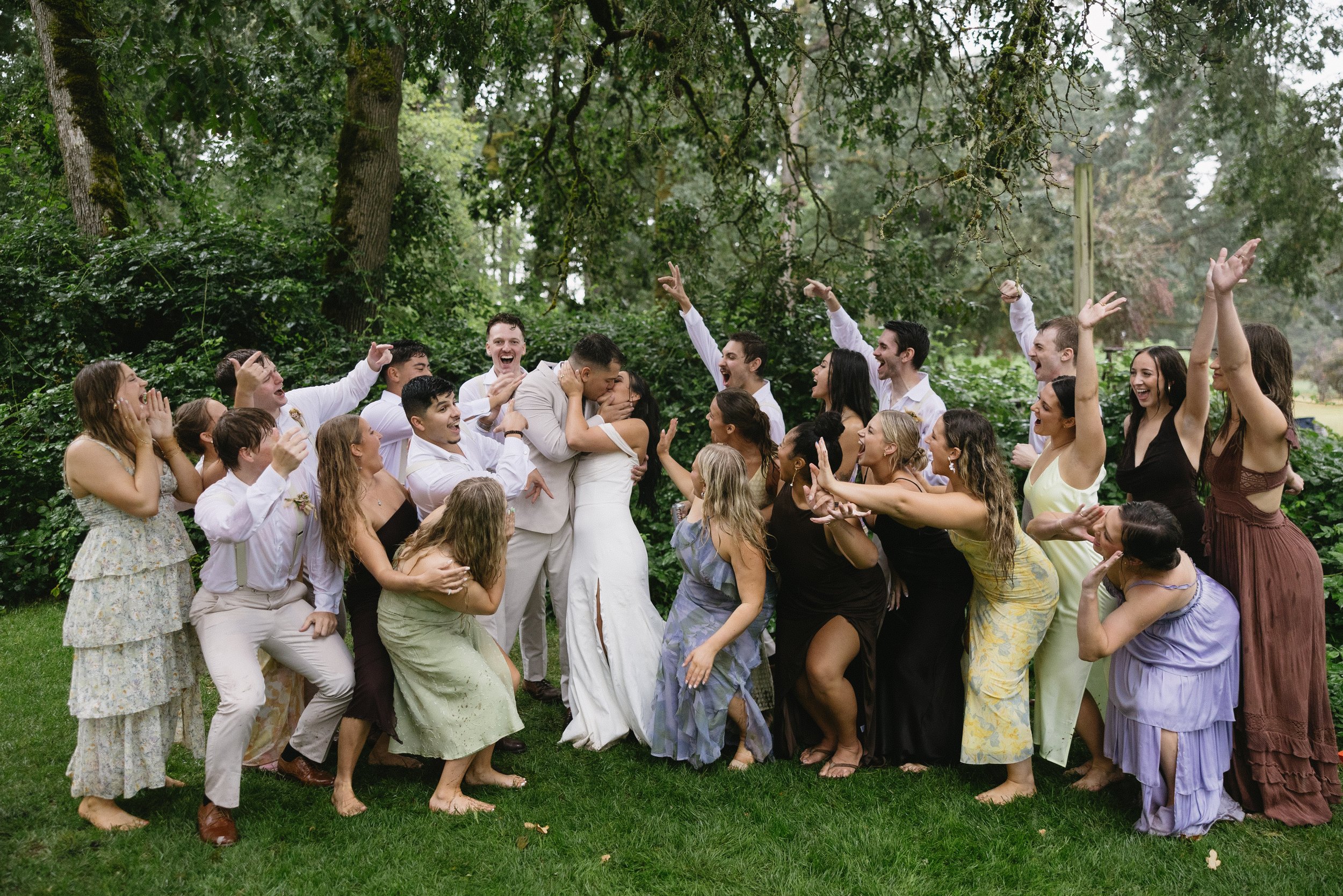 Group of people celebrating outdoors, hugging, and cheering under trees, at a wedding or gathering.