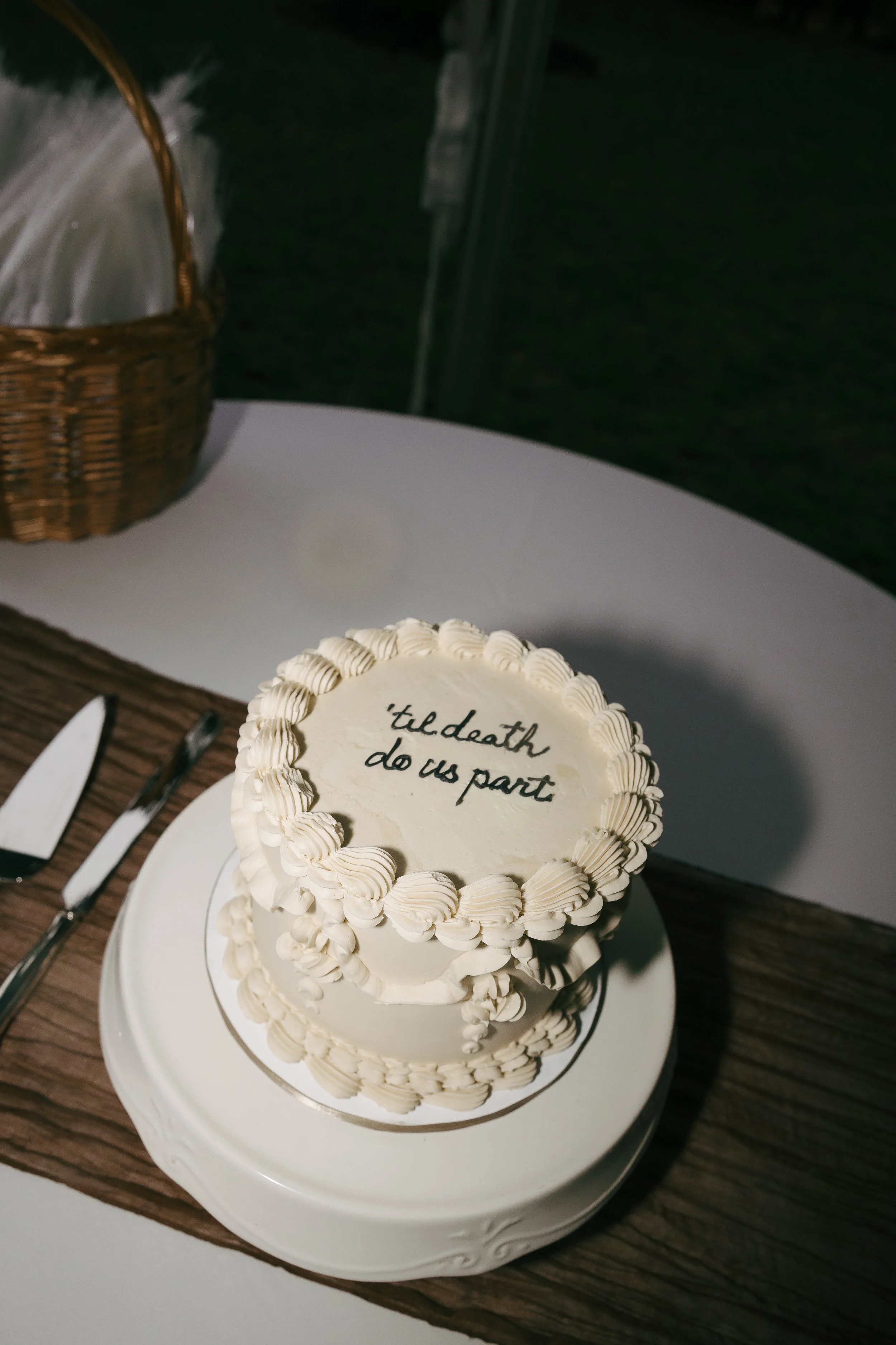 Wedding cake with the message 'til death do us part' written on top, decorated with white icing and piped border.