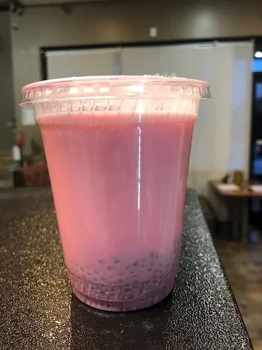 A cup of pink bubble tea with tapioca pearls at the bottom, placed on a black surface in a cafe setting.