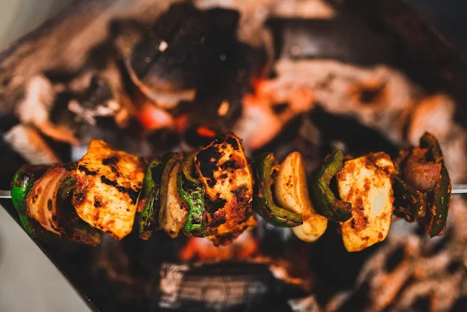Close-up of a grilled vegetable and chicken skewer in front of a charcoal grill.