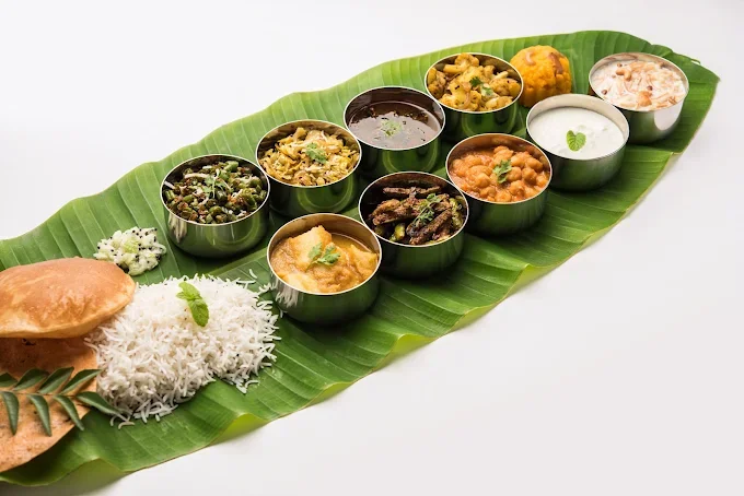 Assorted Indian dishes served on a banana leaf with rice, bread, and small bowls of various curries and side dishes.