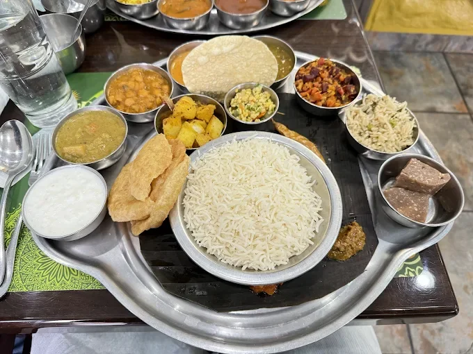Traditional Indian Thali with various curries, rice, bread, and condiments on a metal tray.