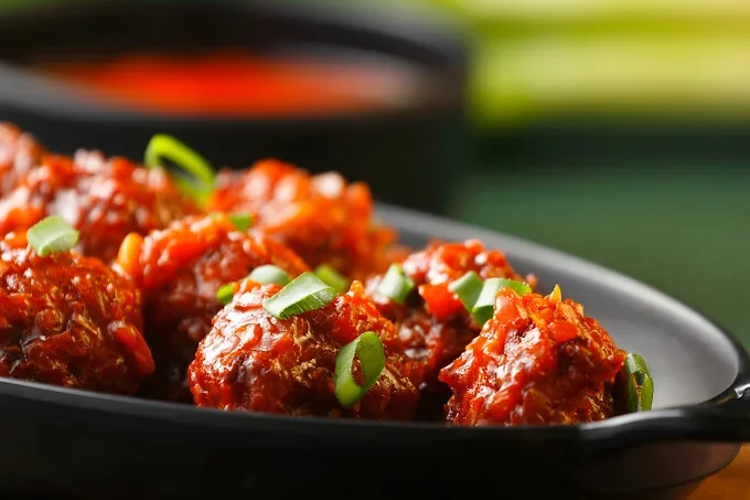 Close-up of meatballs with tomato sauce and chopped green onions in a black dish.