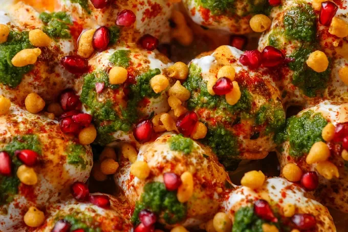 Close-up of a plate of spicy, garnished popcorn with green herbs, red chili powder, pomegranate seeds, and yellow chickpeas.