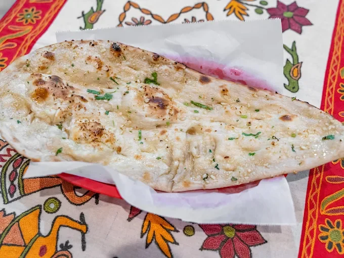 A grilled fish fillet with chopped herbs resting on a piece of white paper on a colorful tablecloth.