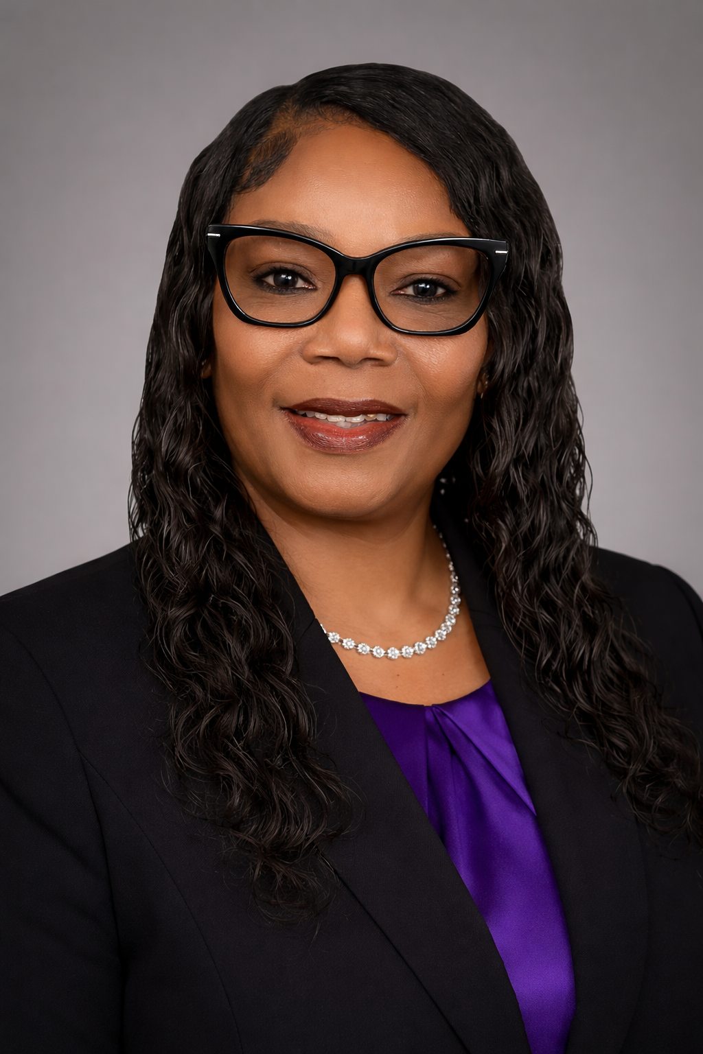 Professional headshot of an African American woman wearing glasses, a black blazer, a purple blouse, and a pearl necklace, smiling at the camera.