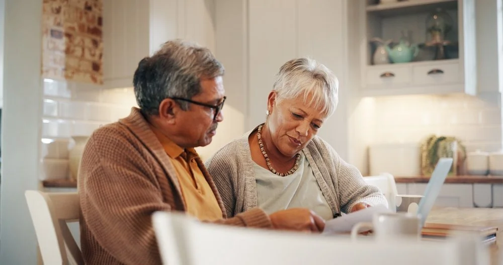 A retired couple reviewing bank statements and residency paperwork at their kitchen table