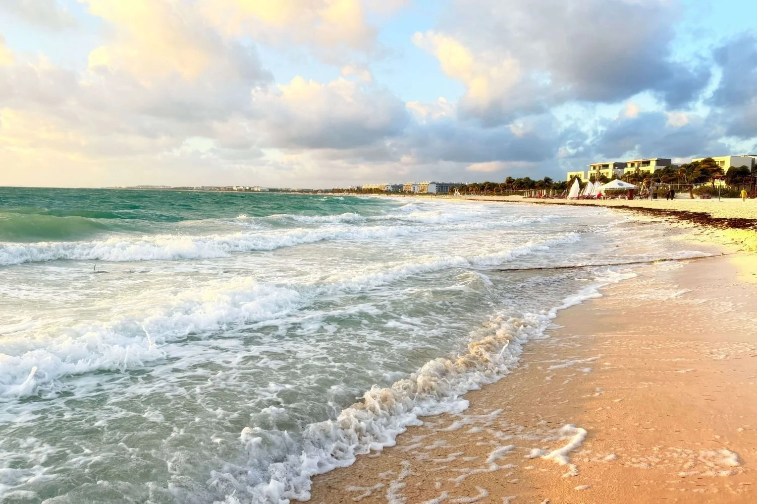 Beach in Playa del Carmen at sunset with waves and beachfront buildings along the shore