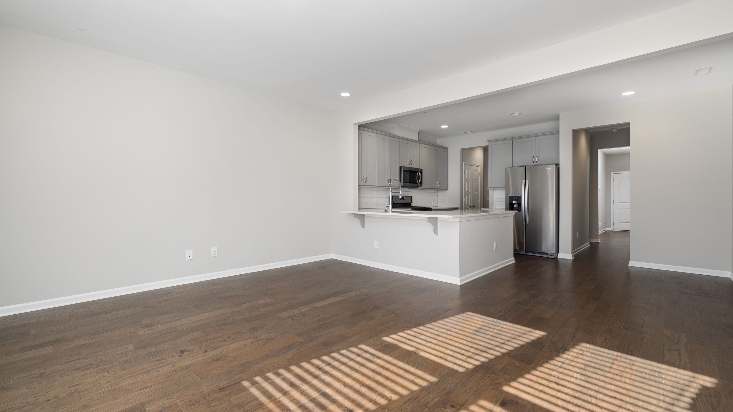 Empty open-plan apartment with sunlight on a wooden floor and a small kitchen at the far end