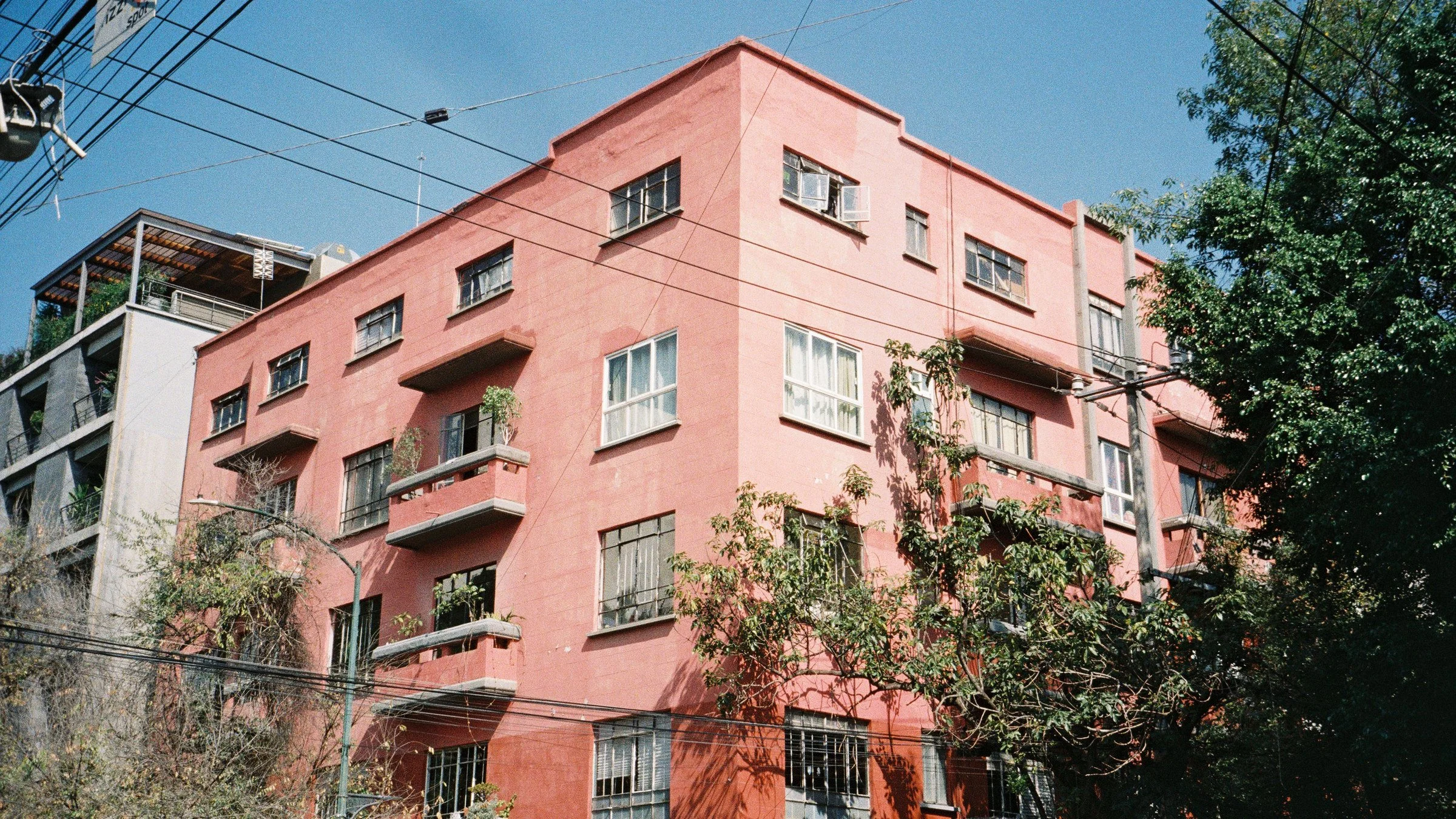 Pink mid-century apartment block with small balconies and trees under a blue sky in Mexico City
