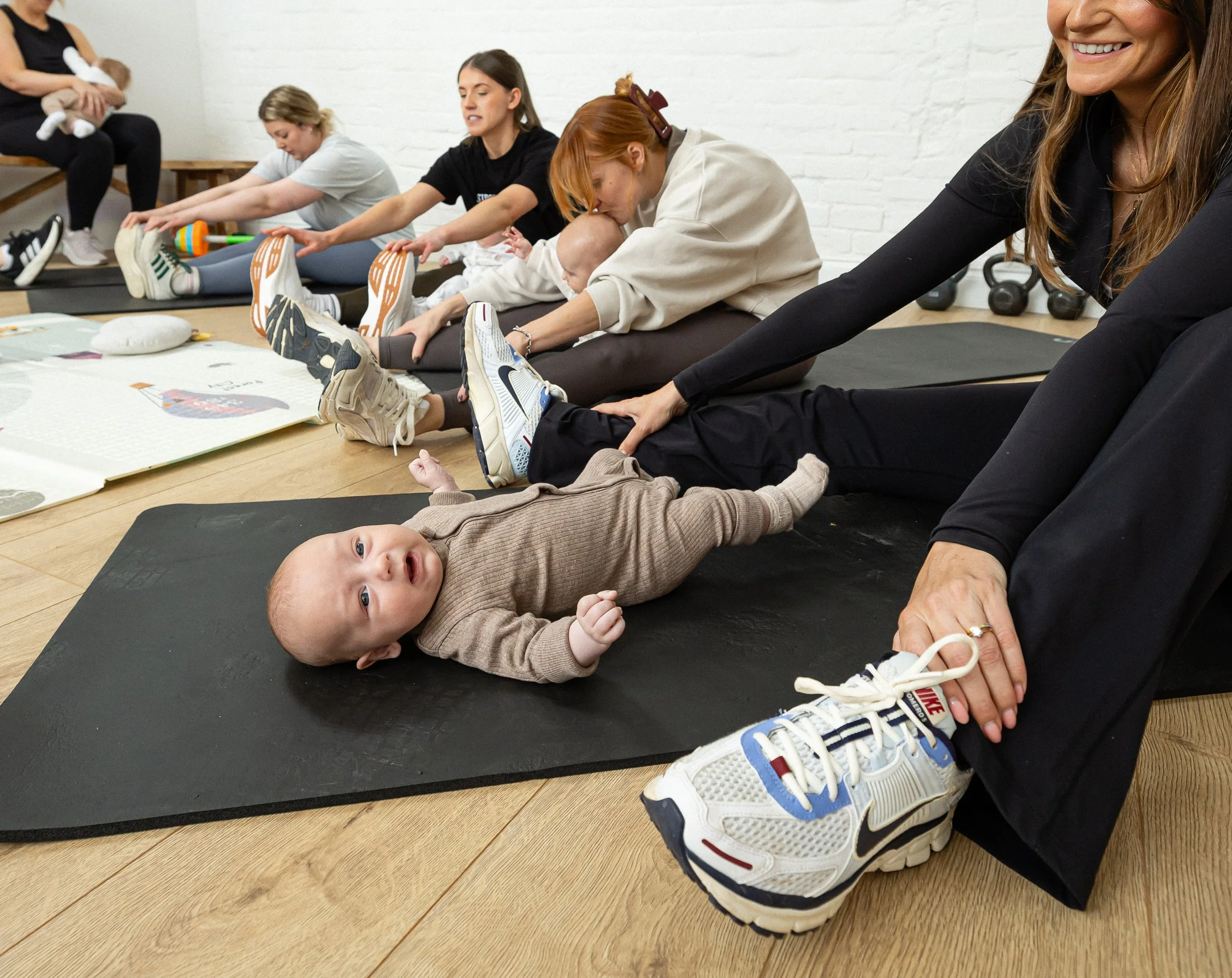 Group of women and children stretching on yoga mats in a fitness studio.