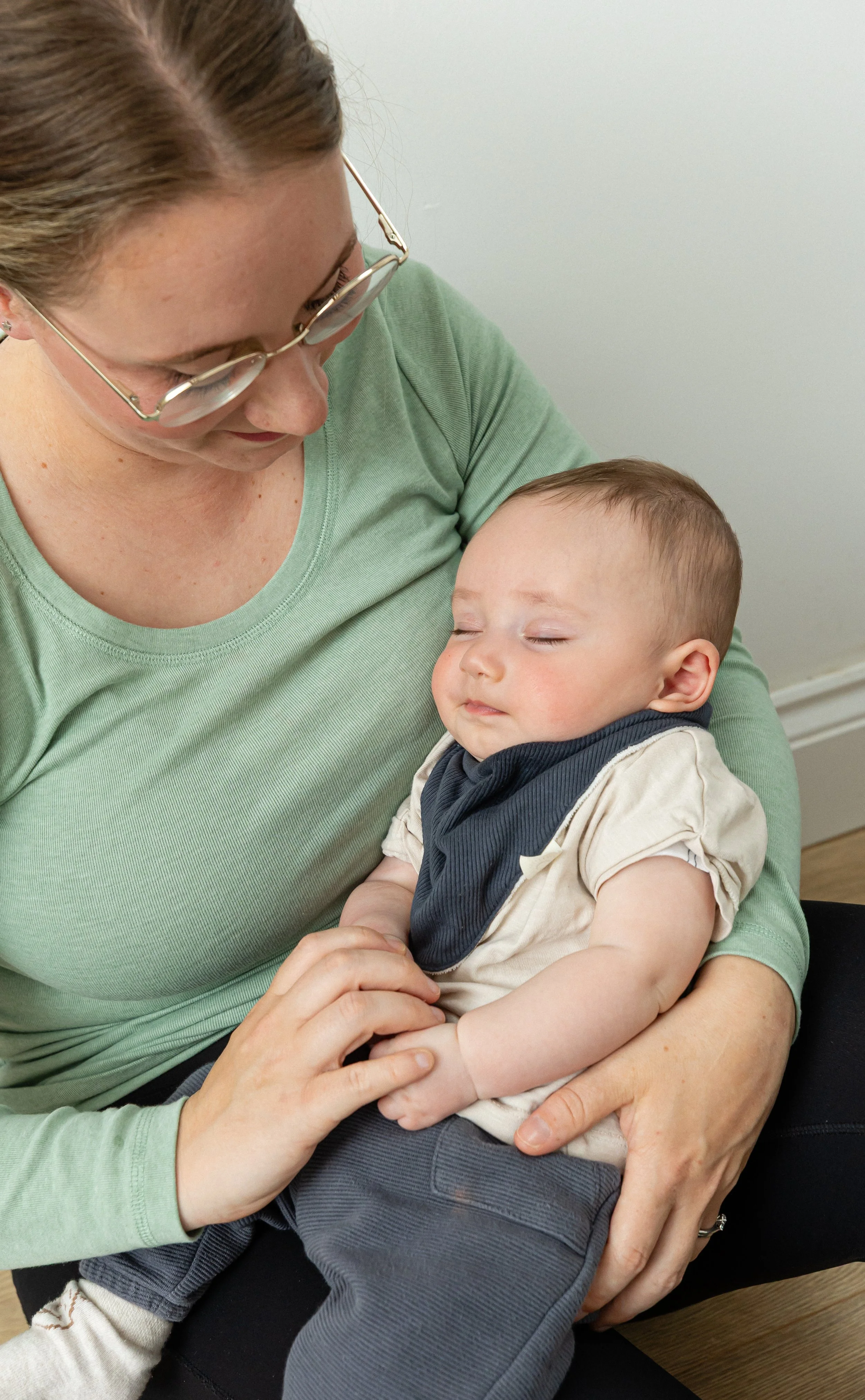 A woman with glasses holding a sleeping young boy in her arms.