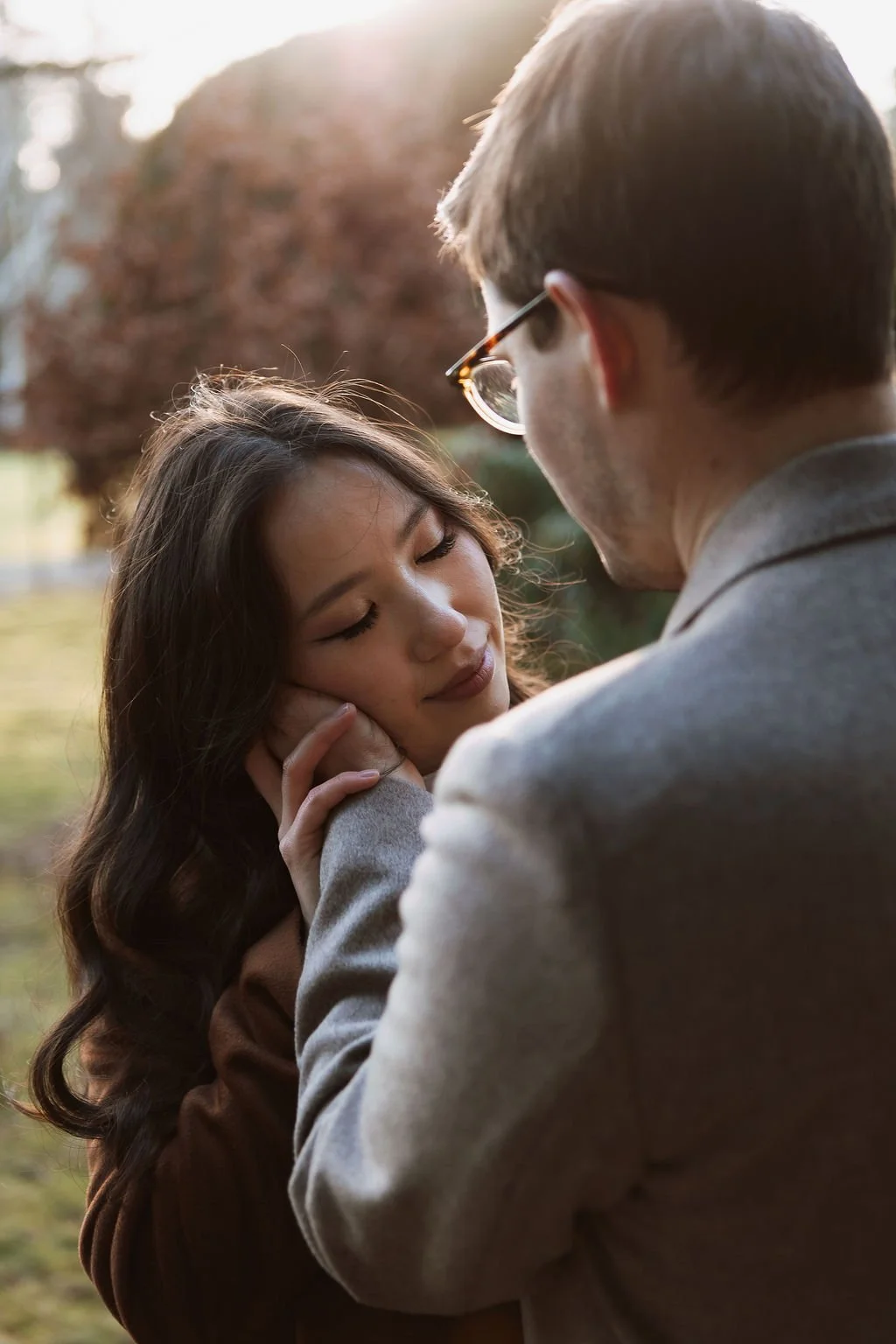 A man and woman sharing an intimate moment outdoors, with the woman gently touching the man's face and eyes closed, during sunset.