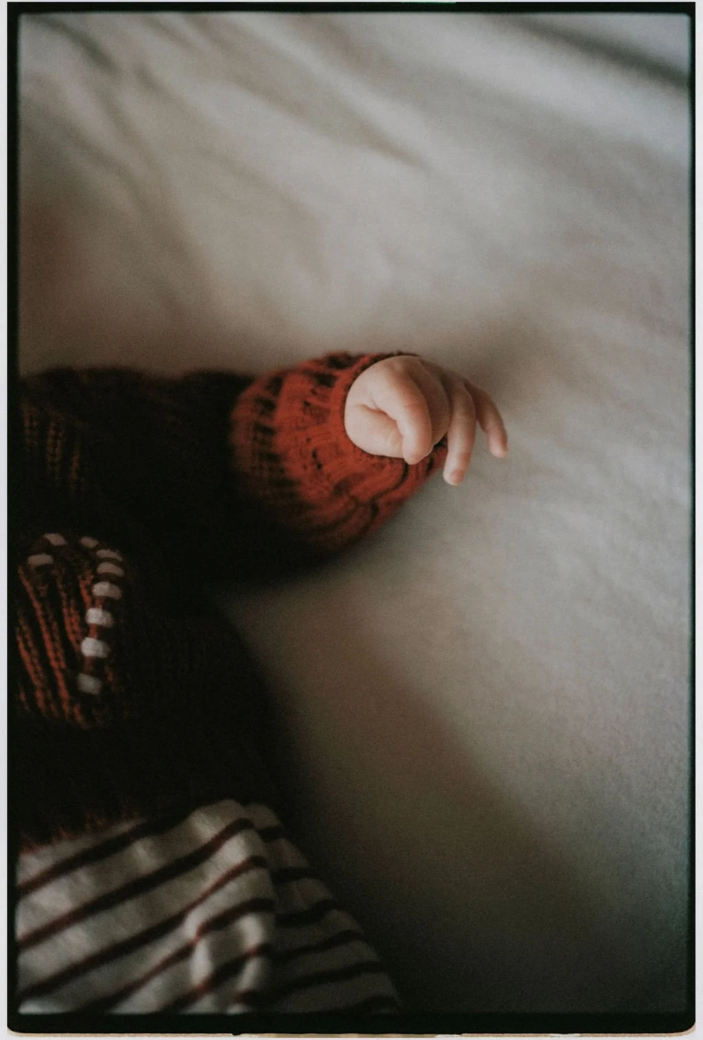 Close-up of a baby's hand with chubby fingers, wearing a red and black sweater, resting on a light-colored surface.