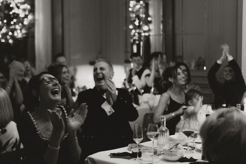 People sitting at a banquet table, laughing and clapping during a celebration or party.