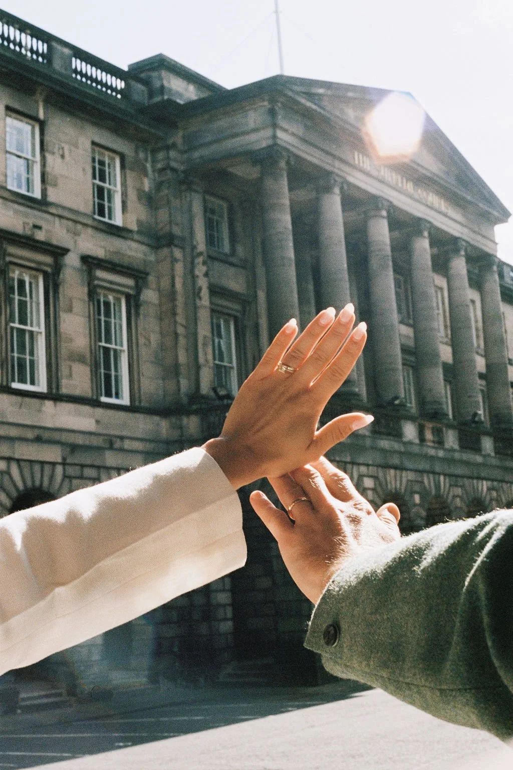 Two people high-fiving in front of a historic building with large columns and multiple windows, sunlight overhead.