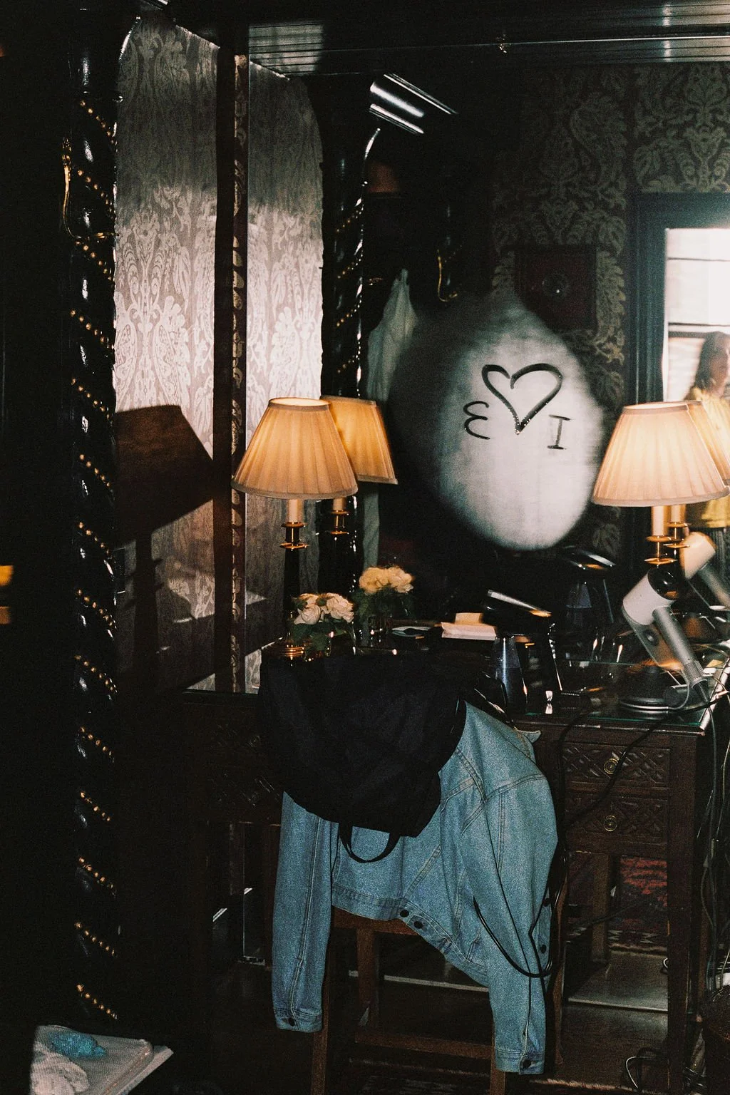 Decorative indoor space with lamps, a large gray vase with black writing and a heart, flowers, and a person's reflection in a mirror.