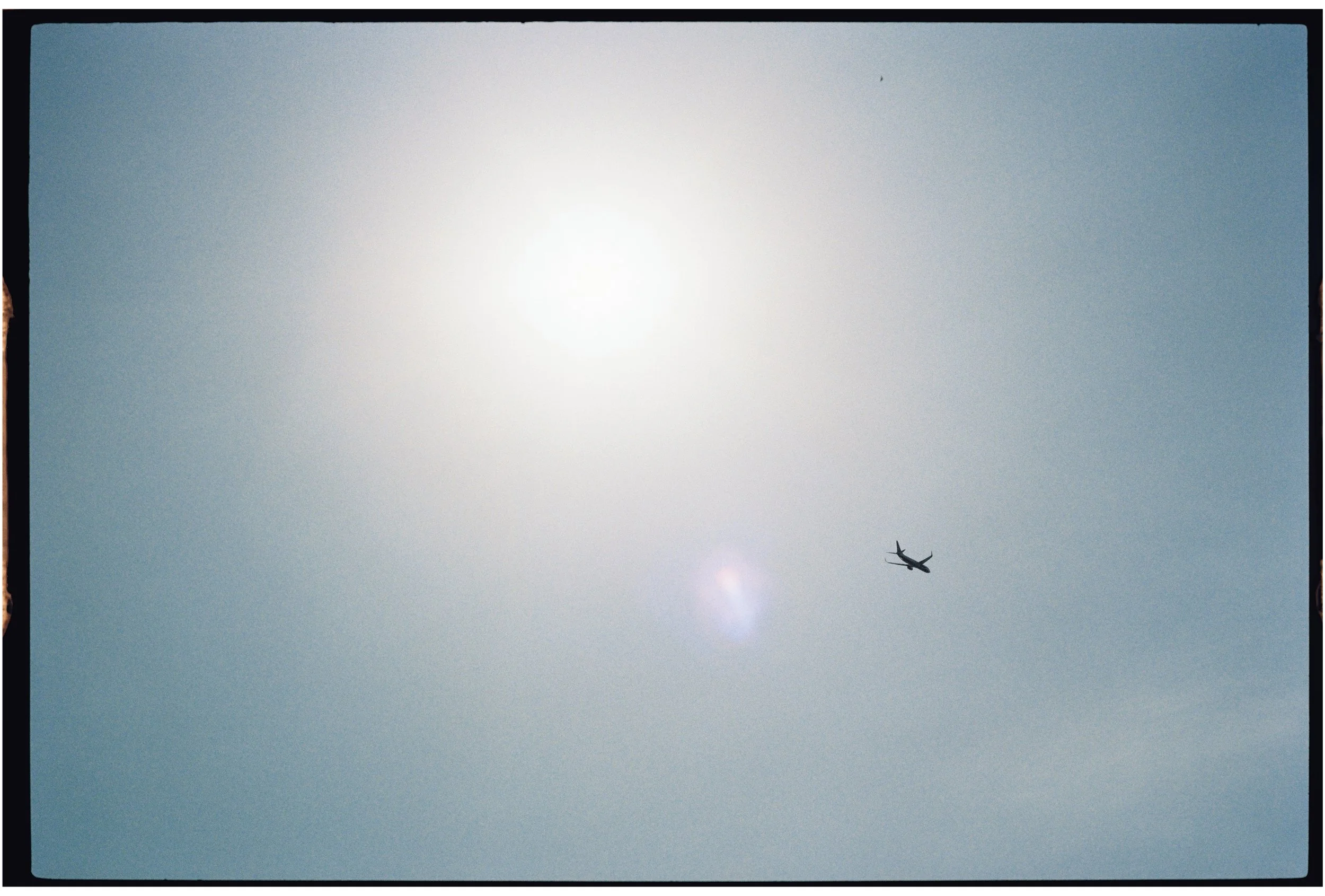 A plane flying in a clear sky near the sun. Photographed on 35mm film.