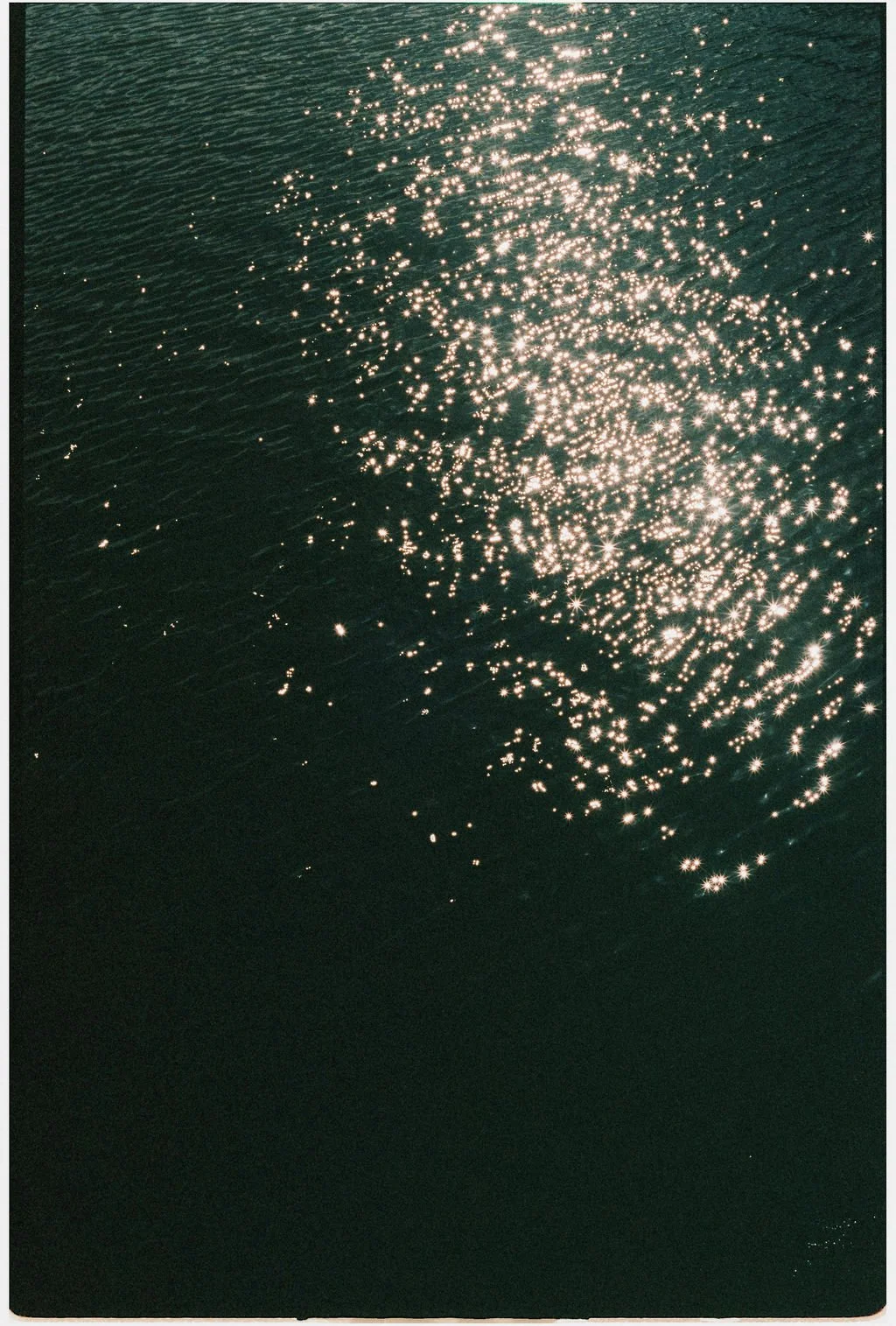 Sunlight reflecting off the water creating bright, sparkling highlights on a dark surface, possibly a body of water such as a lake or ocean.