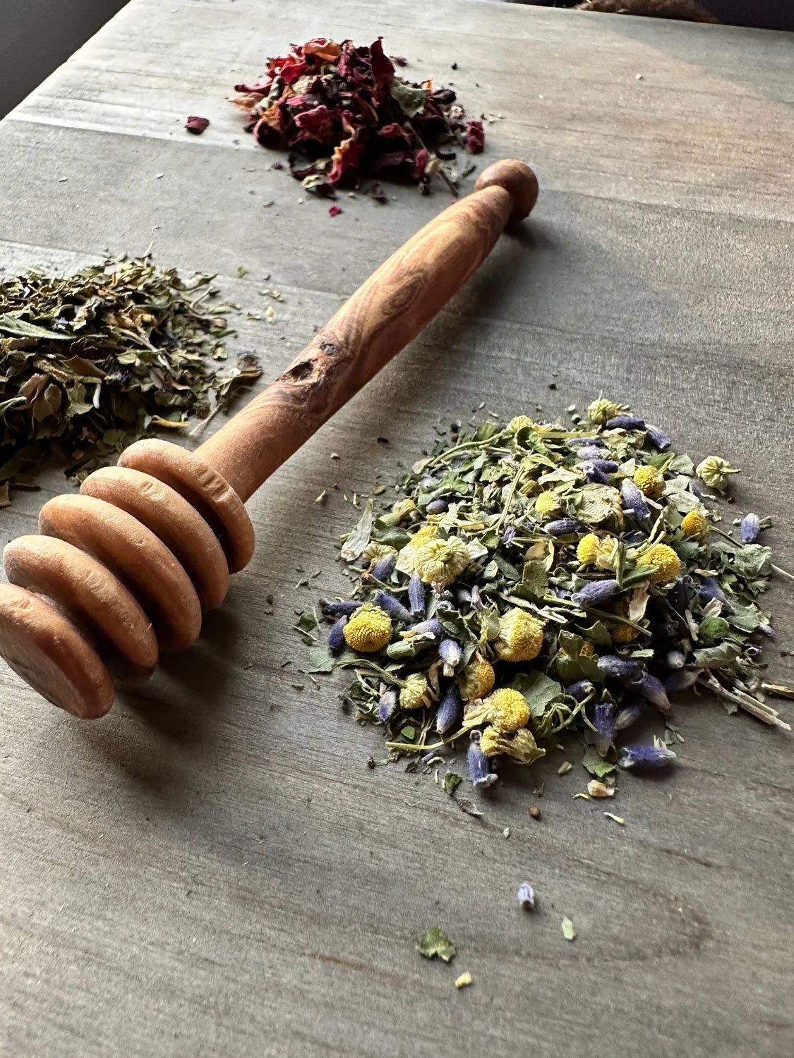 Asheville locally-sourced dried herbs and flowers on a wooden surface with a wooden honey dipper