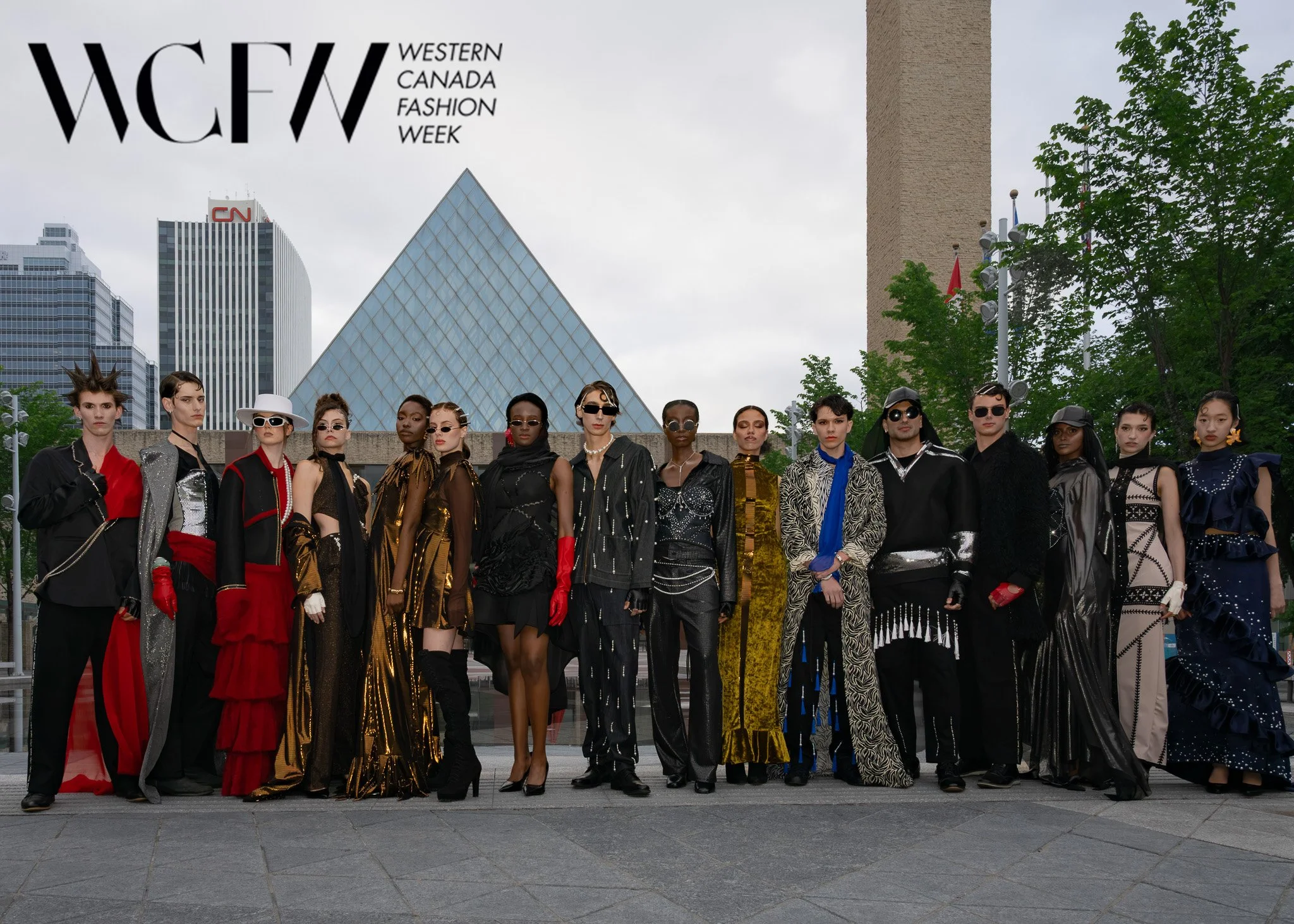 Group of diverse fashion models standing together outdoors, dressed in high-fashion outfits with a city skyline in the background, during Western Canada Fashion Week.