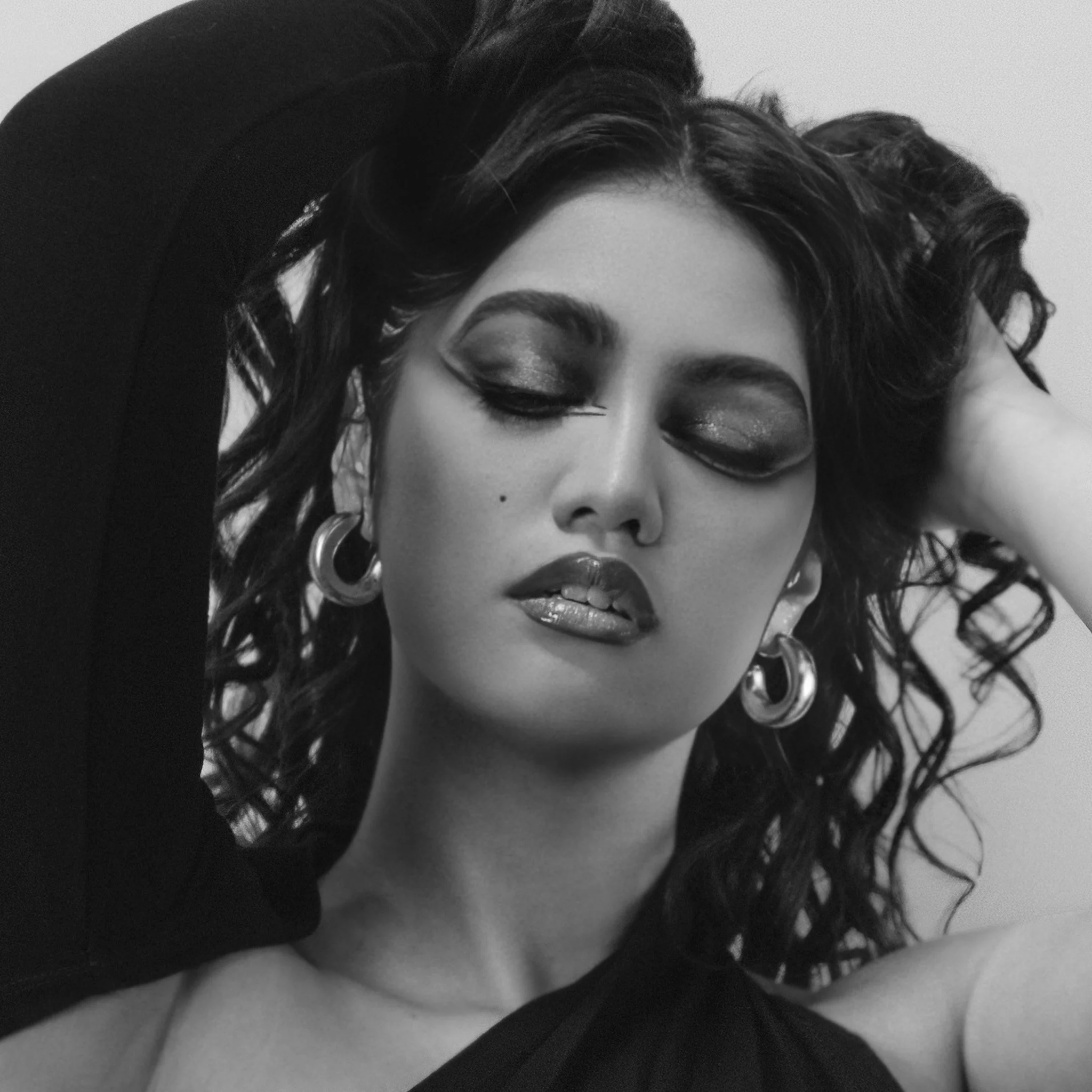 A black and white close-up photo of a woman's face with curly hair, wearing earrings, with her eyes closed and head tilted back.