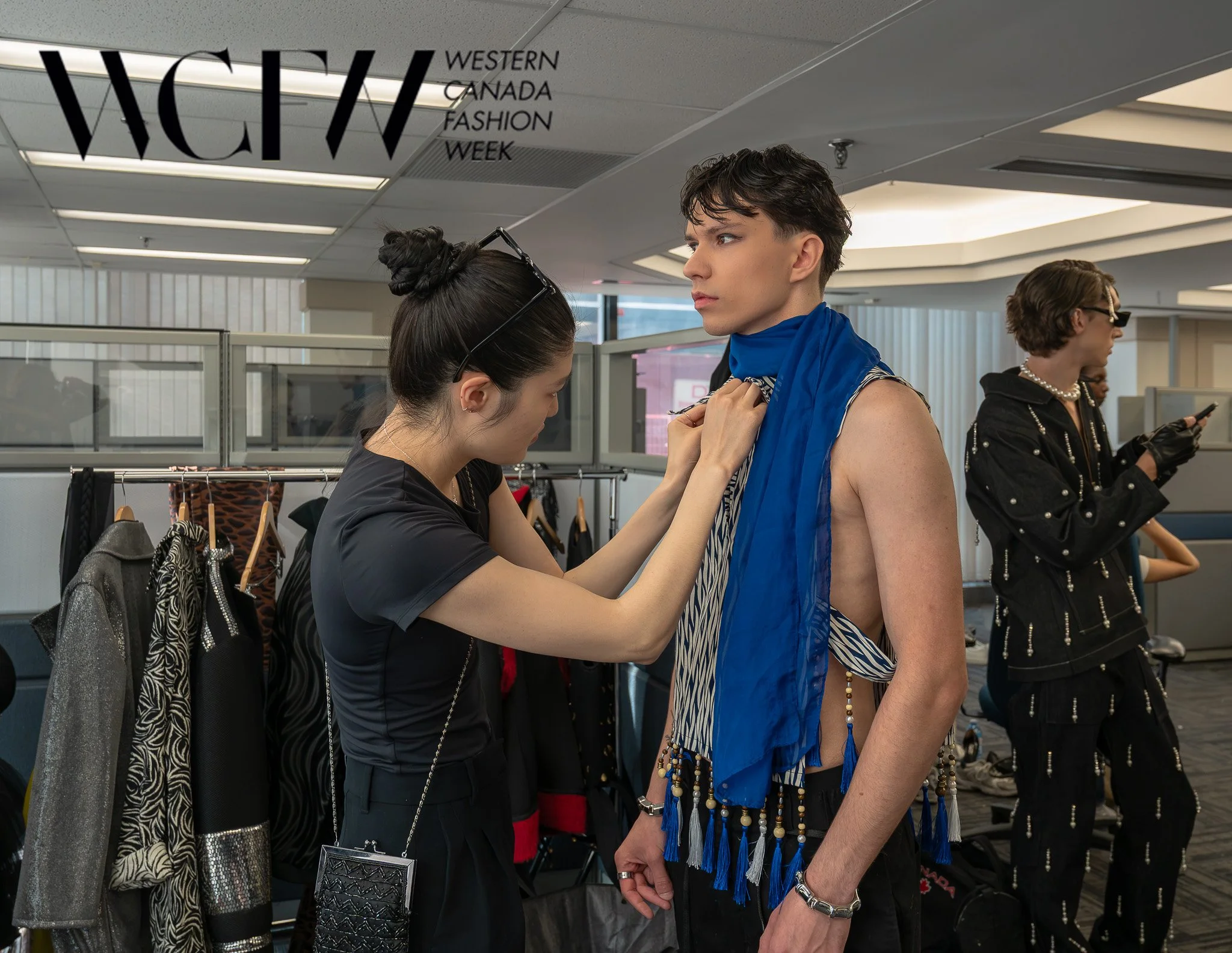 A model at Western Canada Fashion Week getting ready backstage, with a stylist adjusting her outfit.