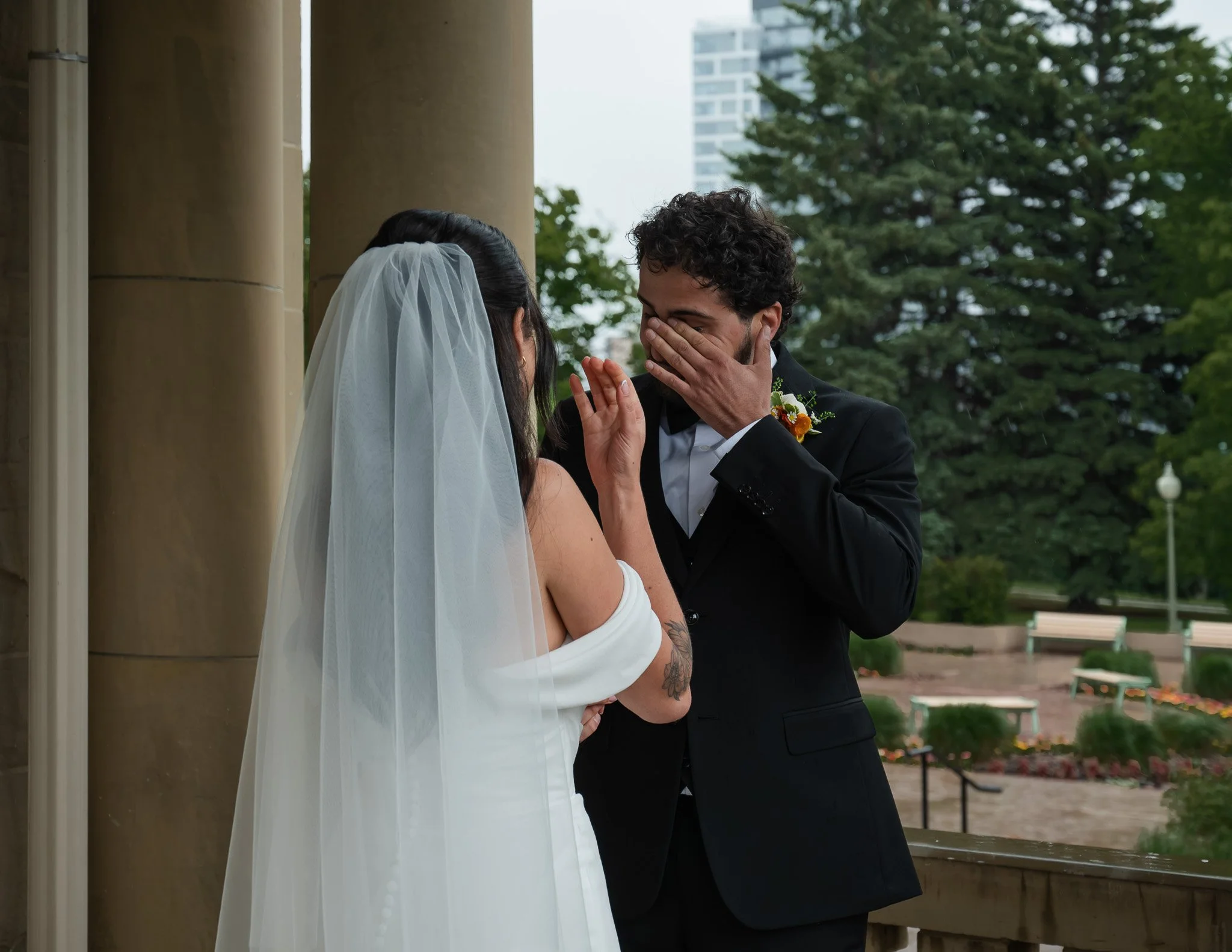 A bride and groom sharing an emotional moment outdoors during their wedding ceremony, with the groom touching the bride's face and both looking into each other's eyes.