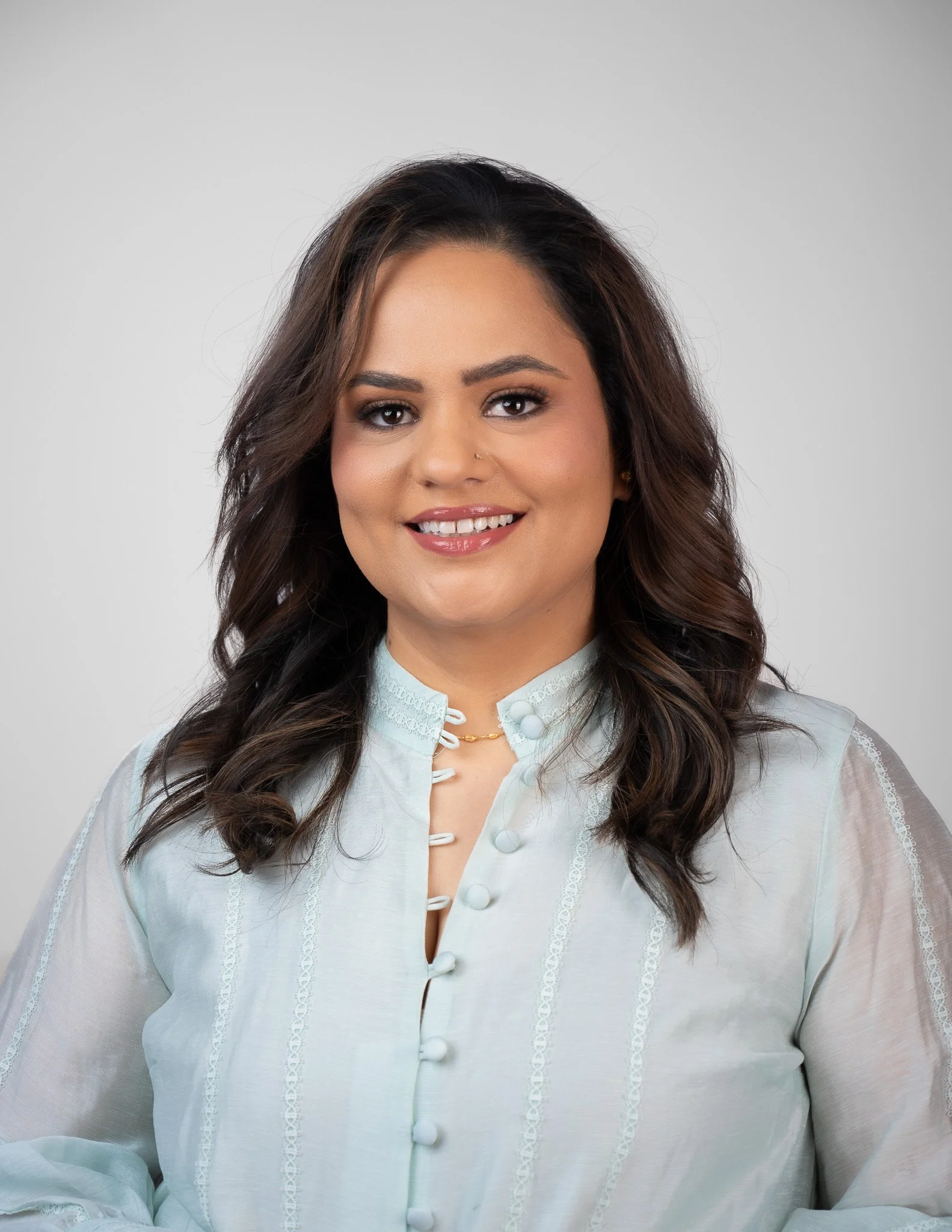 Headshot Photography Edmonton by Edmonton Headshot Photographer. A woman with dark brown, curly hair and light brown complexion smiling while wearing a light-colored traditional blouse with buttons and lace details.