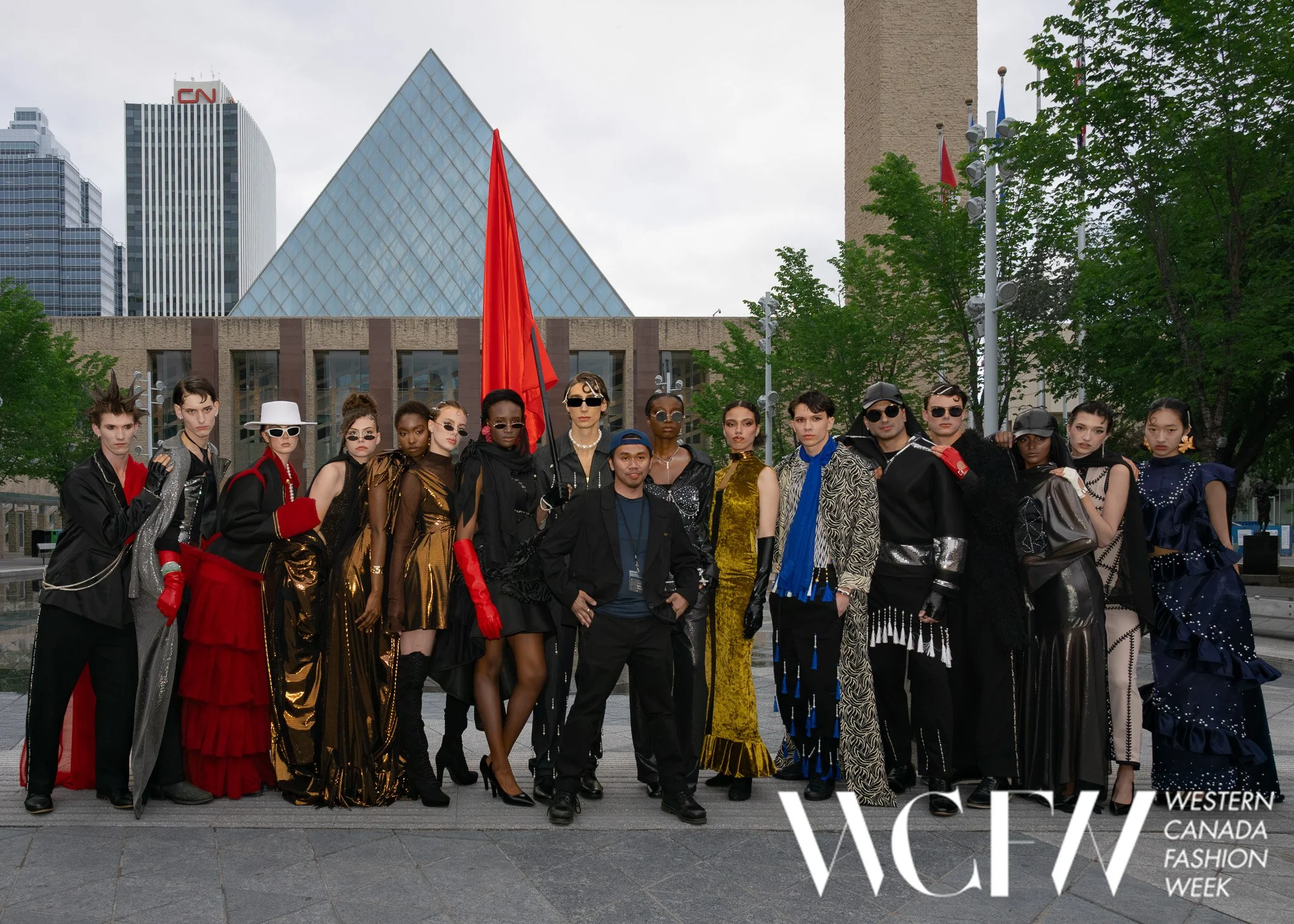 Group of models in fashionable clothing at Western Canada Fashion Week, standing outdoors in front of modern buildings and trees.