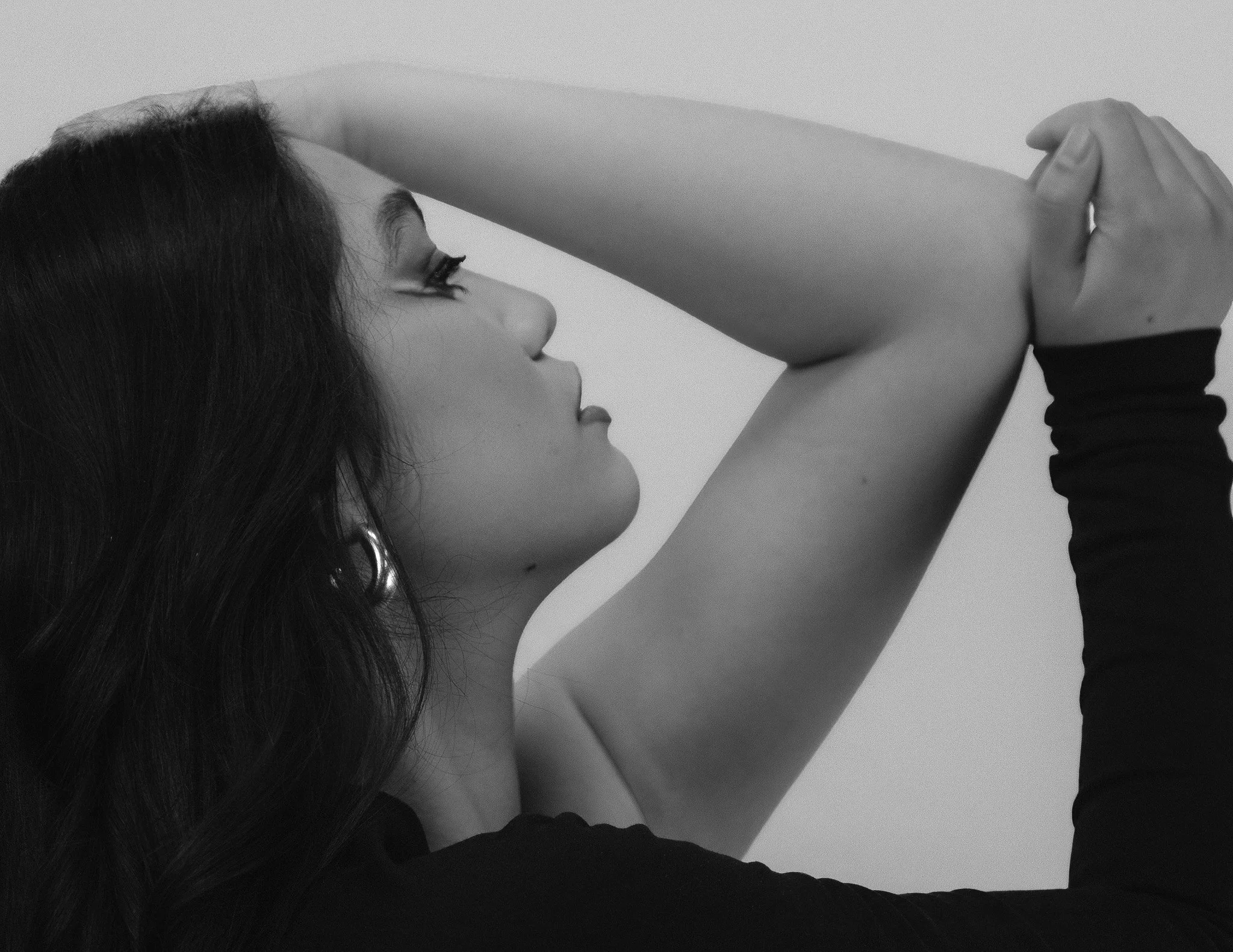 A woman with long dark hair is lying down and looking at her arm as someone else touches her upper arm with their hand. The scene is in black and white.