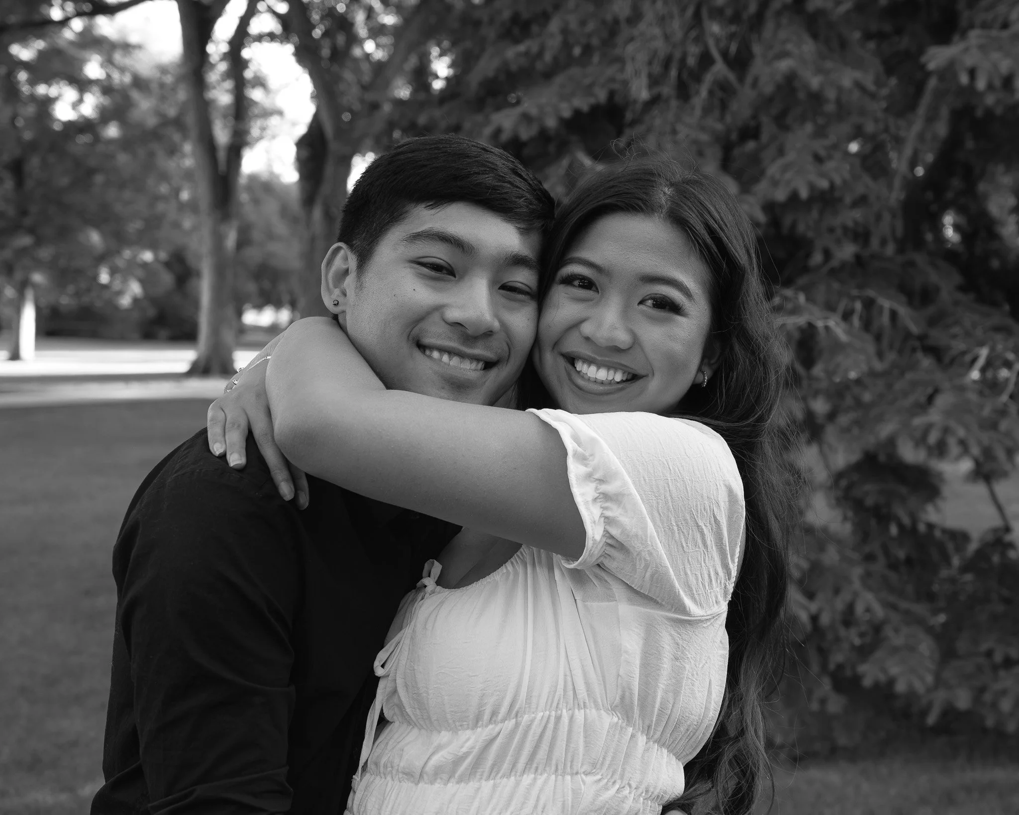 Two people hugging outdoors, smiling, with trees and grass in the background.