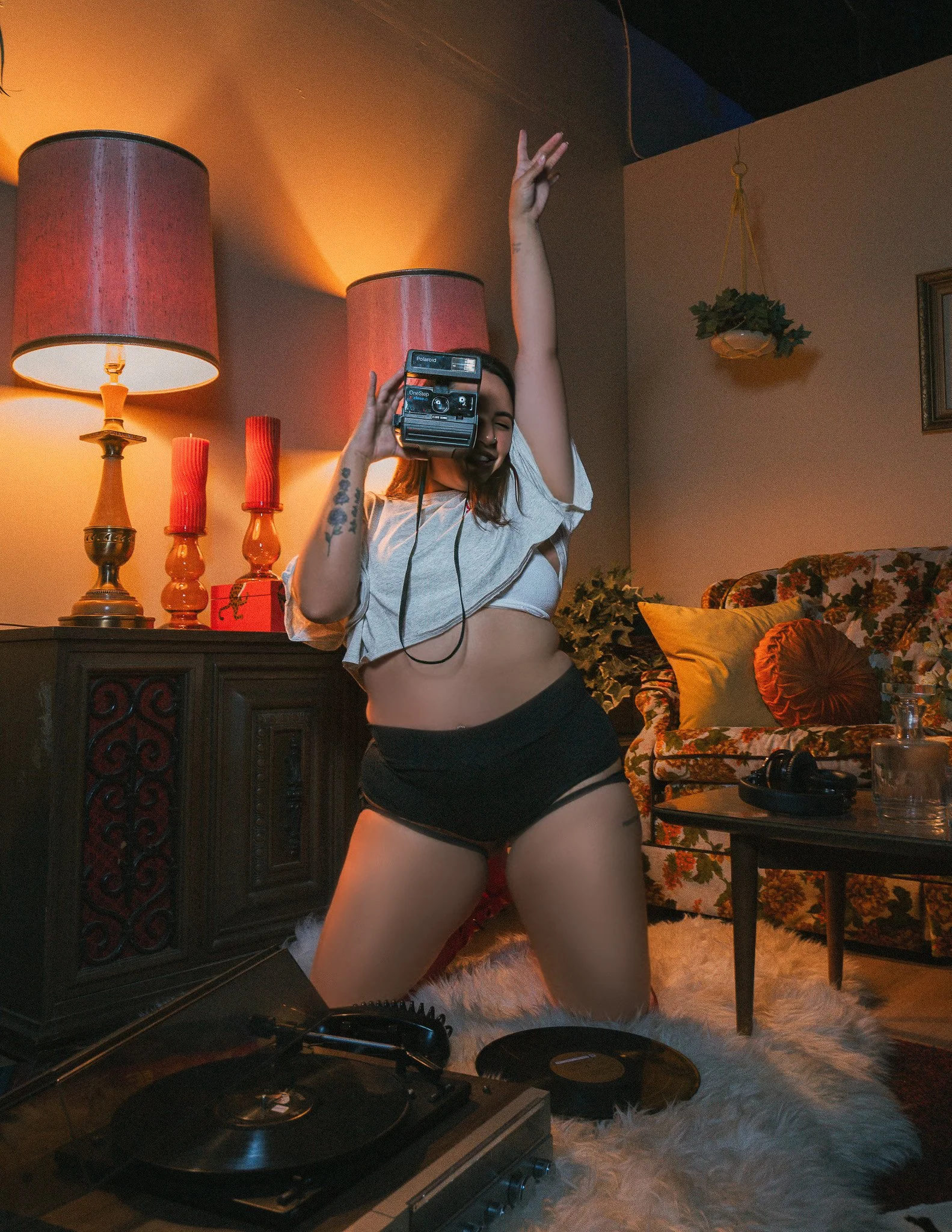 A woman dancing in a cozy living room with warm lighting, floral furniture, and candles on a side table.