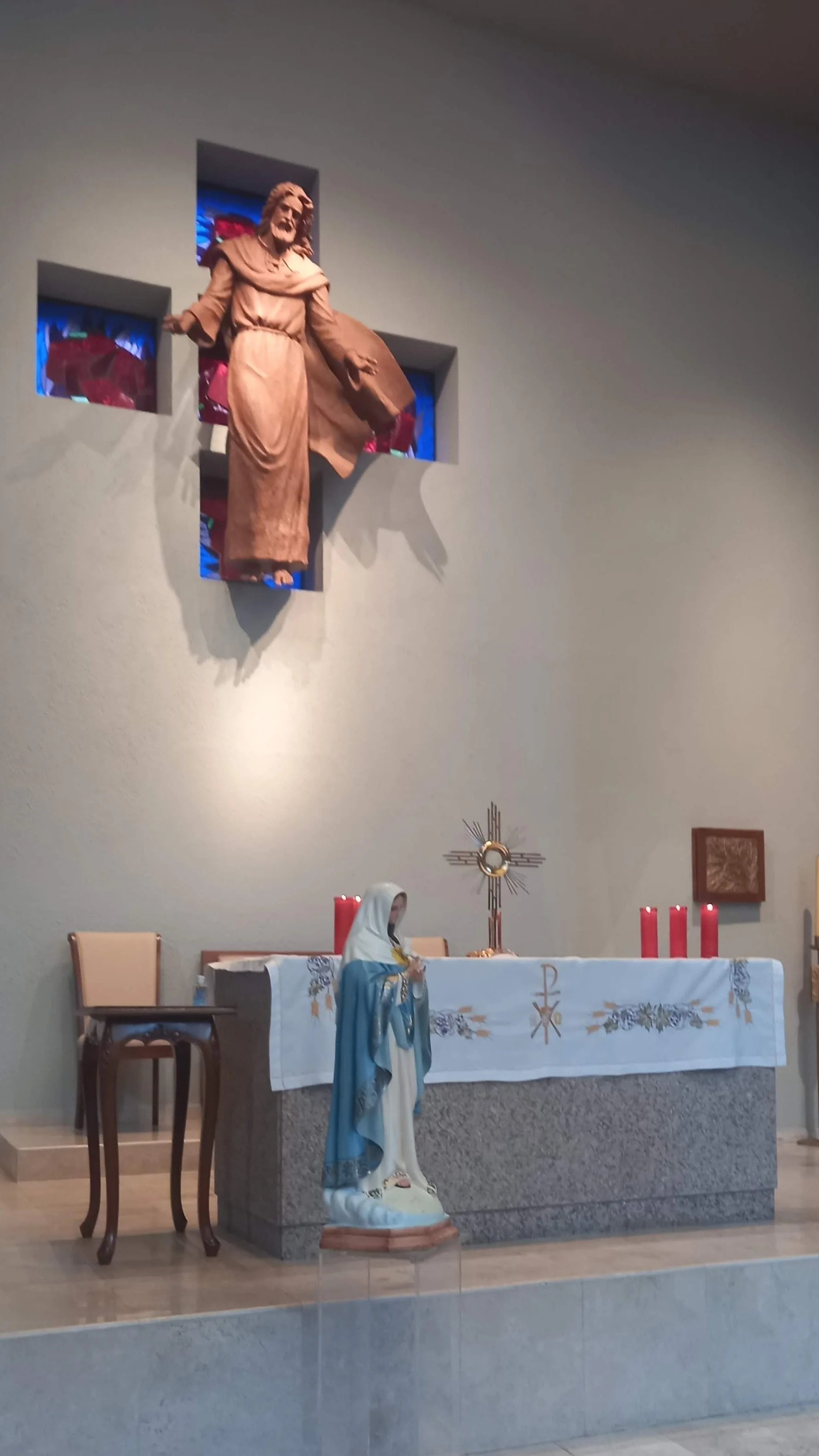 Interior de una iglesia cristiana con altar, estatua de la Virgen María, y figura de Jesús en la cruz en el fondo.