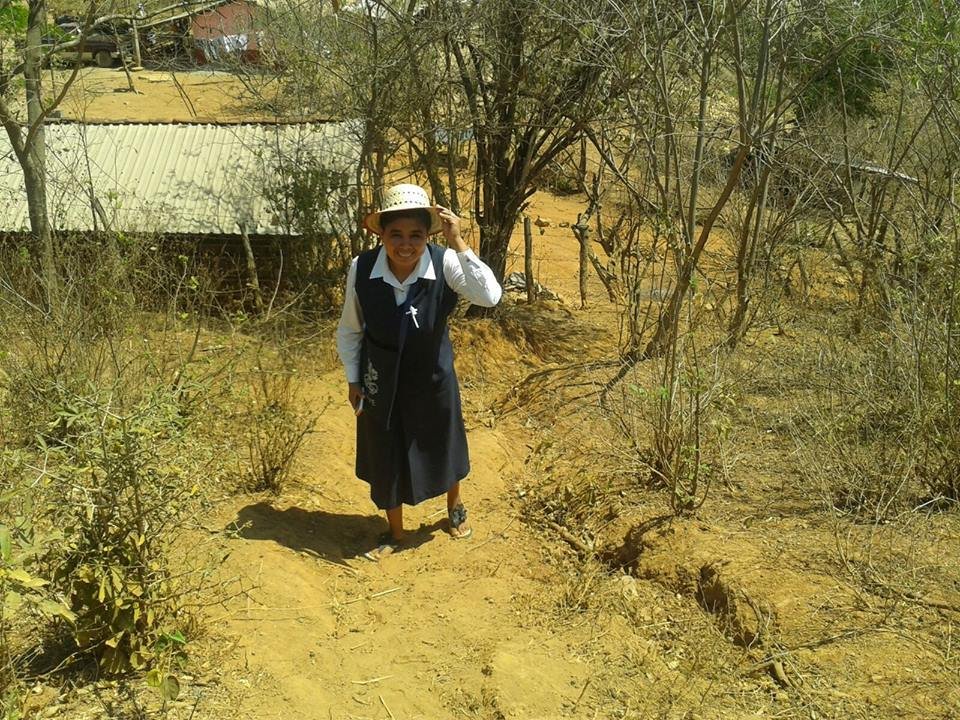 Niña sonriendo con sombrero en un camino de tierra en un ambiente seco y con poco follaje.
