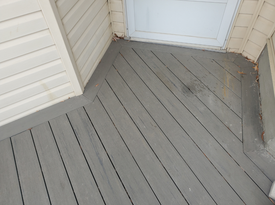 A corner of a wooden deck with a sliding glass door and beige vinyl siding on the house exterior.