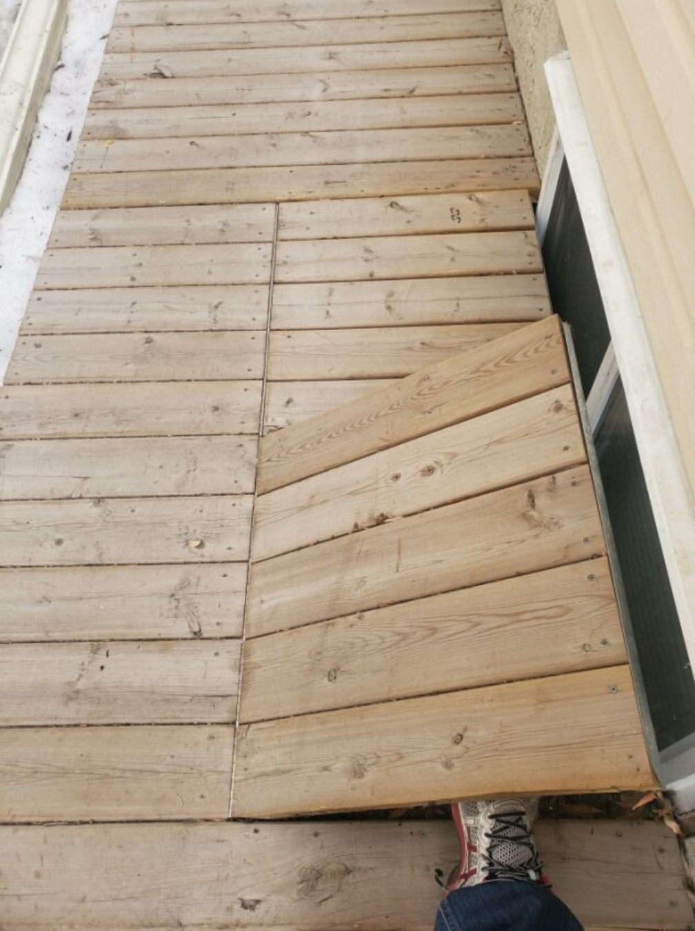 ongoing construction of a wooden deck with partially installed wooden planks, a person's foot visible in the bottom right corner, and building materials nearby.