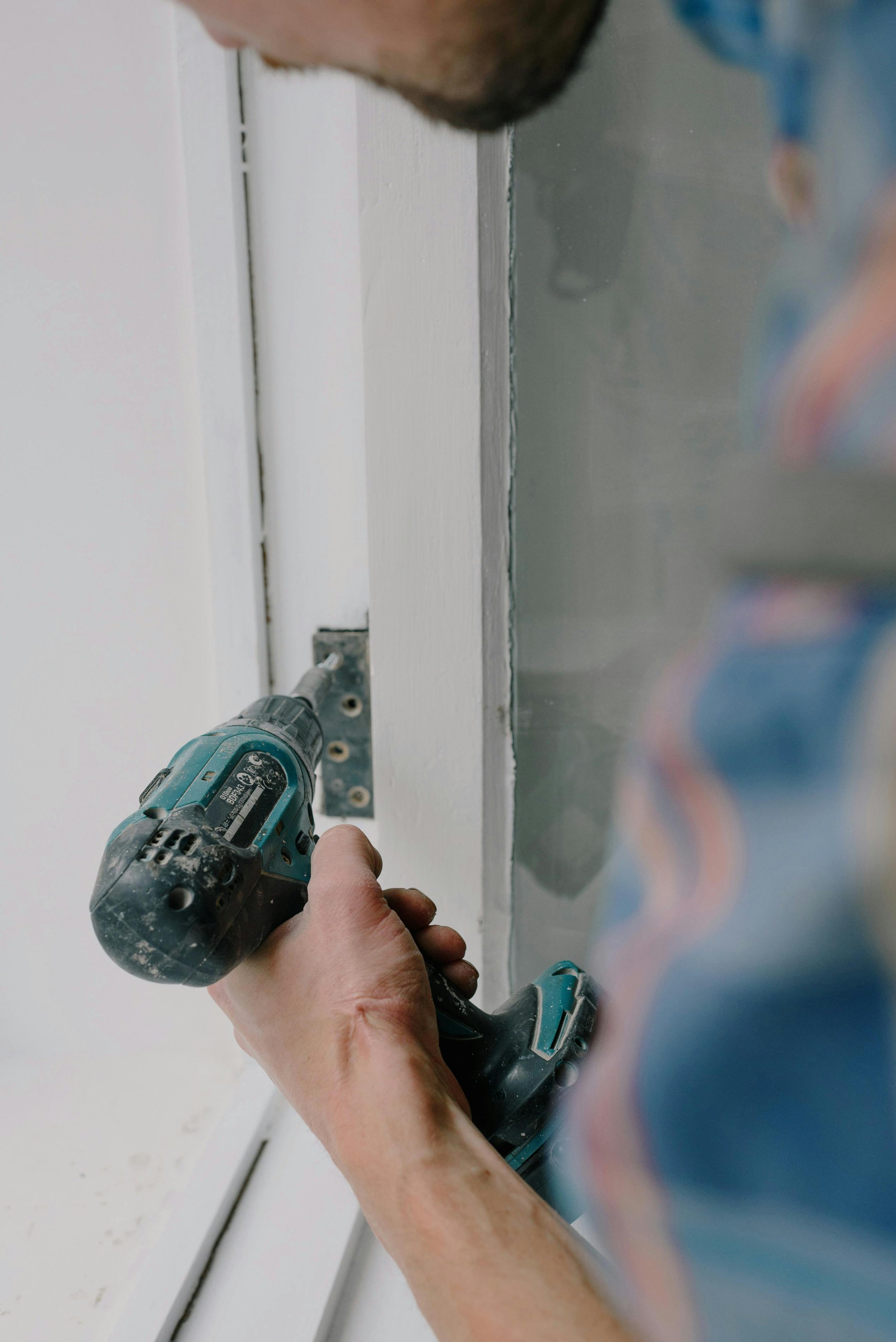Person installing or fixing a door lock or handle using a cordless power drill.