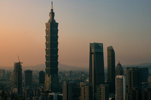 台北101在朦朧的夕陽餘暉中聳立於城市天際線之上，台北