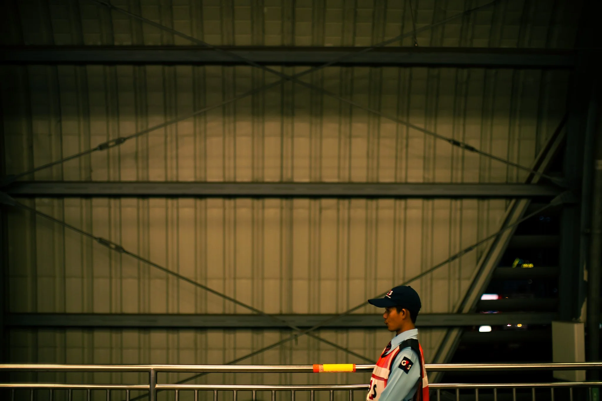 Person in a cap and uniform standing beneath a dark steel overhead structure at night