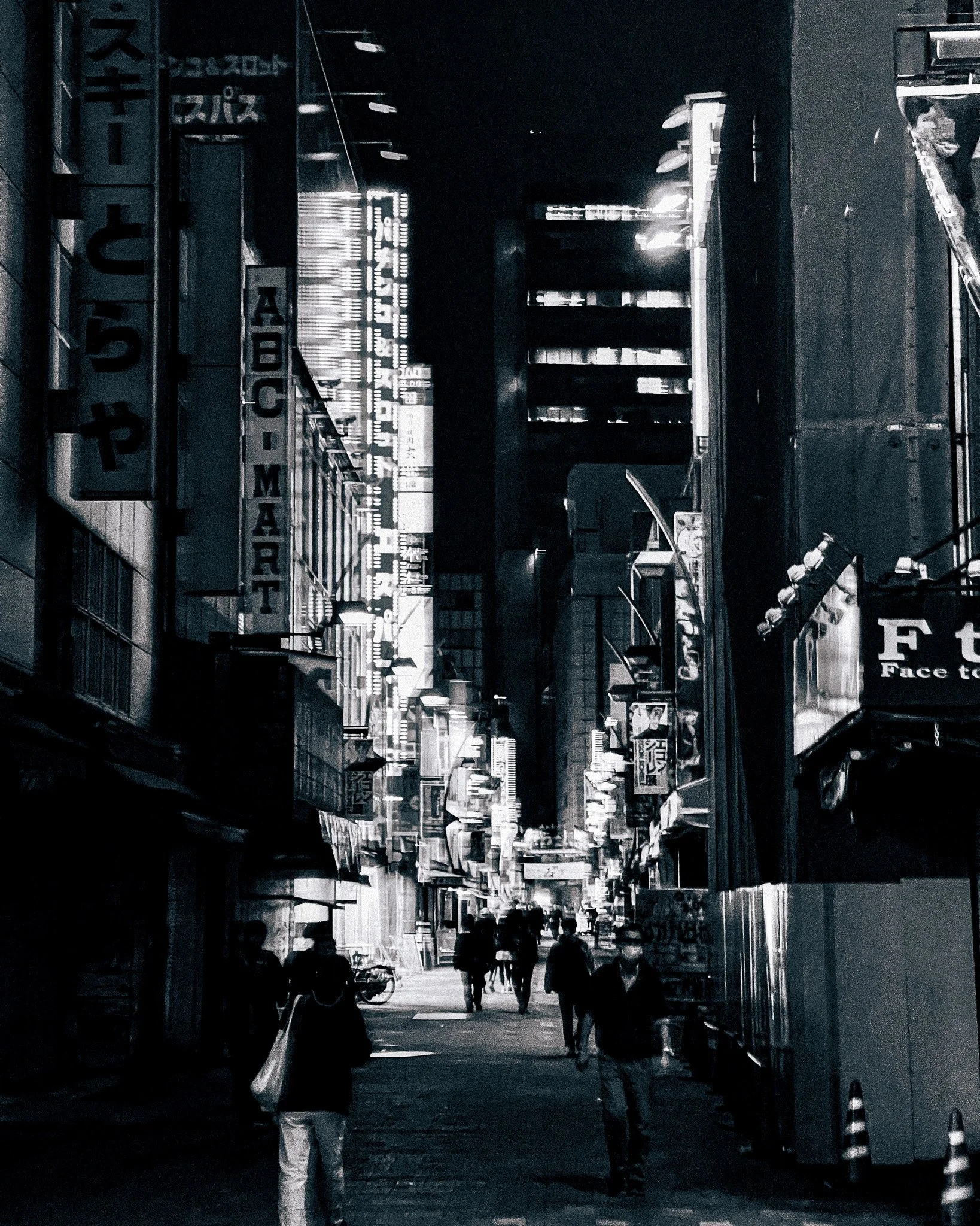 A black and white photo of a busy city street at night with illuminated signs and tall buildings, and people walking.