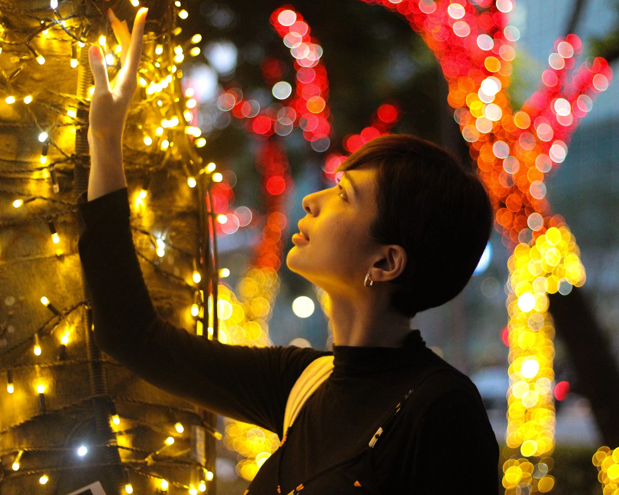Woman decorating a tree with yellow string lights during evening.