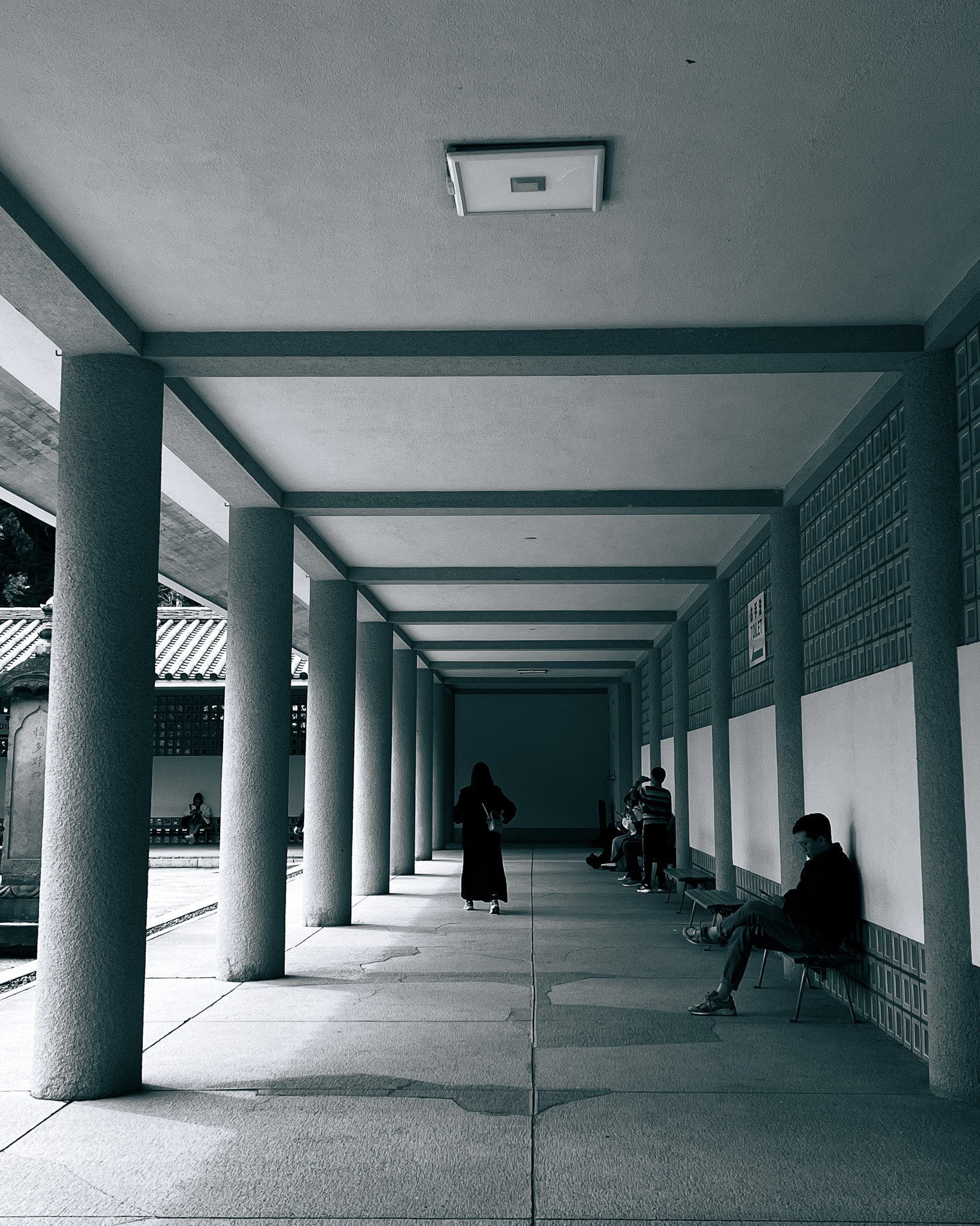 People sitting and standing under a covered walkway with columns, in front of traditional Japanese architecture.