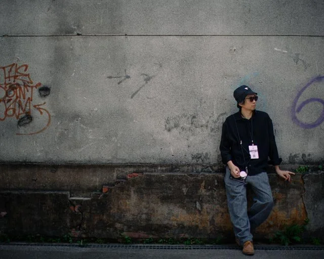 戴漁夫帽與墨鏡的男子倚著佈滿塗鴉的混凝土牆，台灣