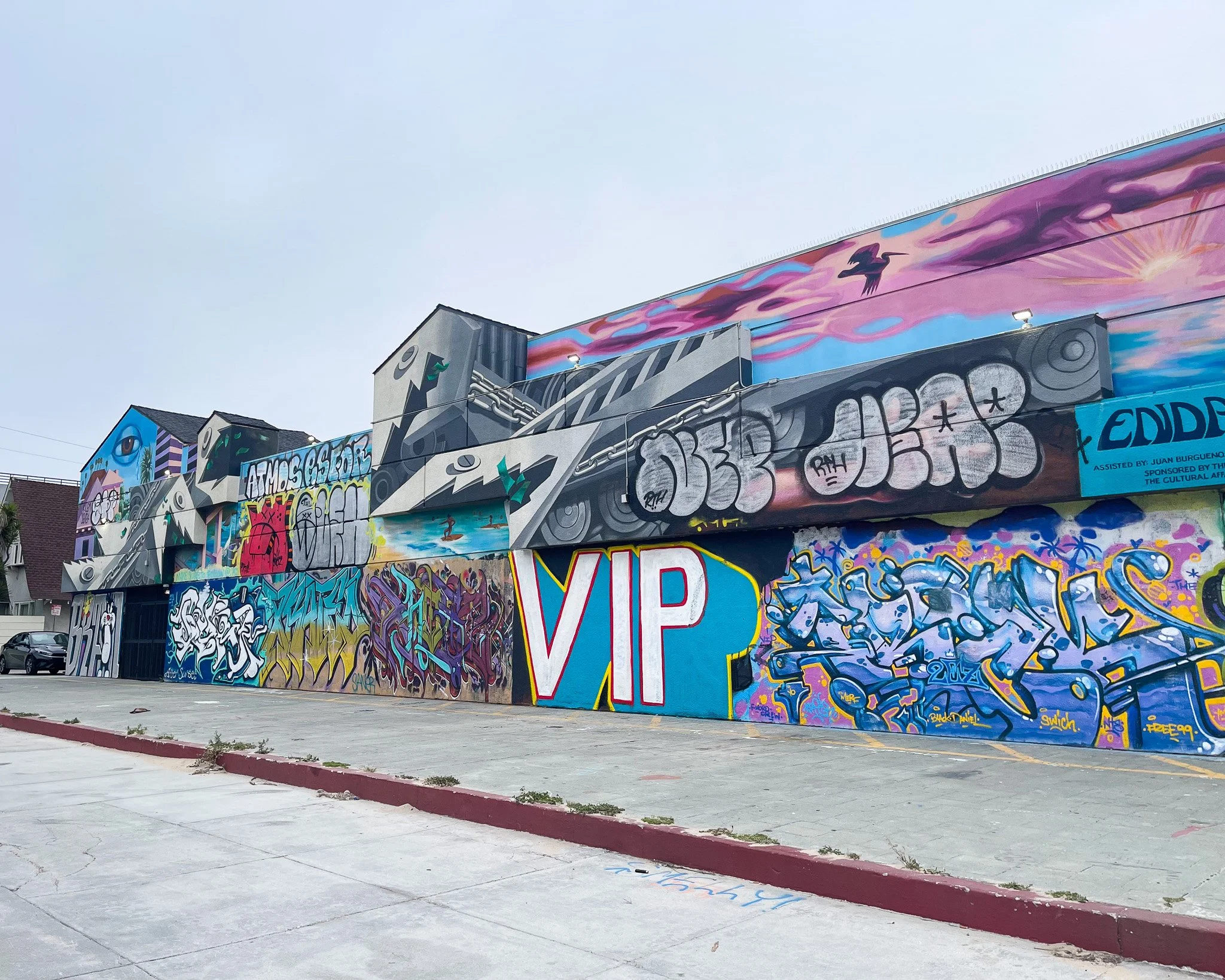 Colorful graffiti murals on a building wall outdoors, featuring various abstract and illustrative designs including eyes, hands, and stylized text, with a large blue and pink VIP sign in the center.