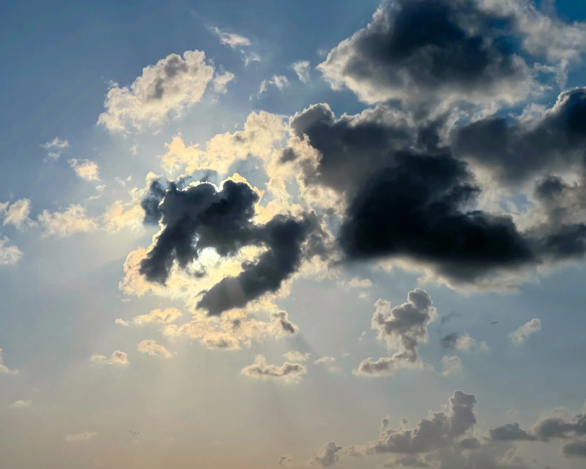 Sky with dark and light clouds, some sunlight shining through.